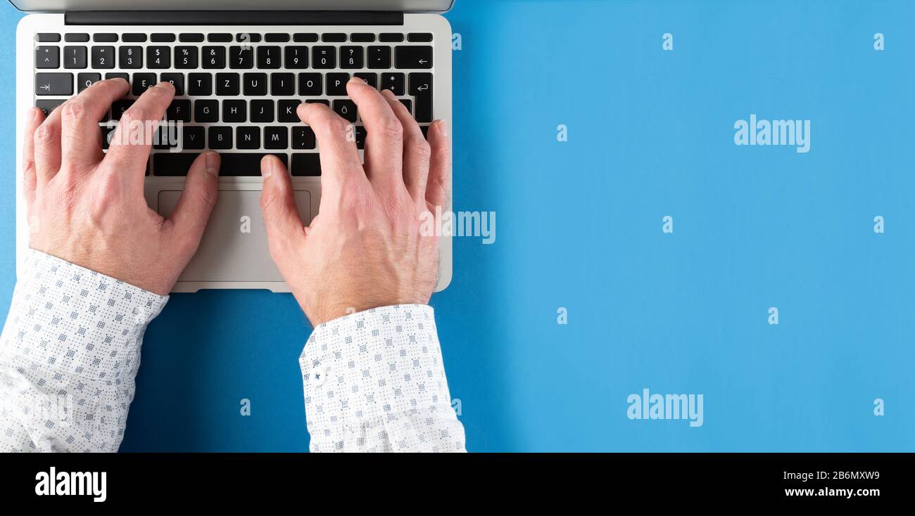 Draufsicht über das Tippen von Männern auf einem Laptop auf blauem Schreibtischhintergrund Stockfoto