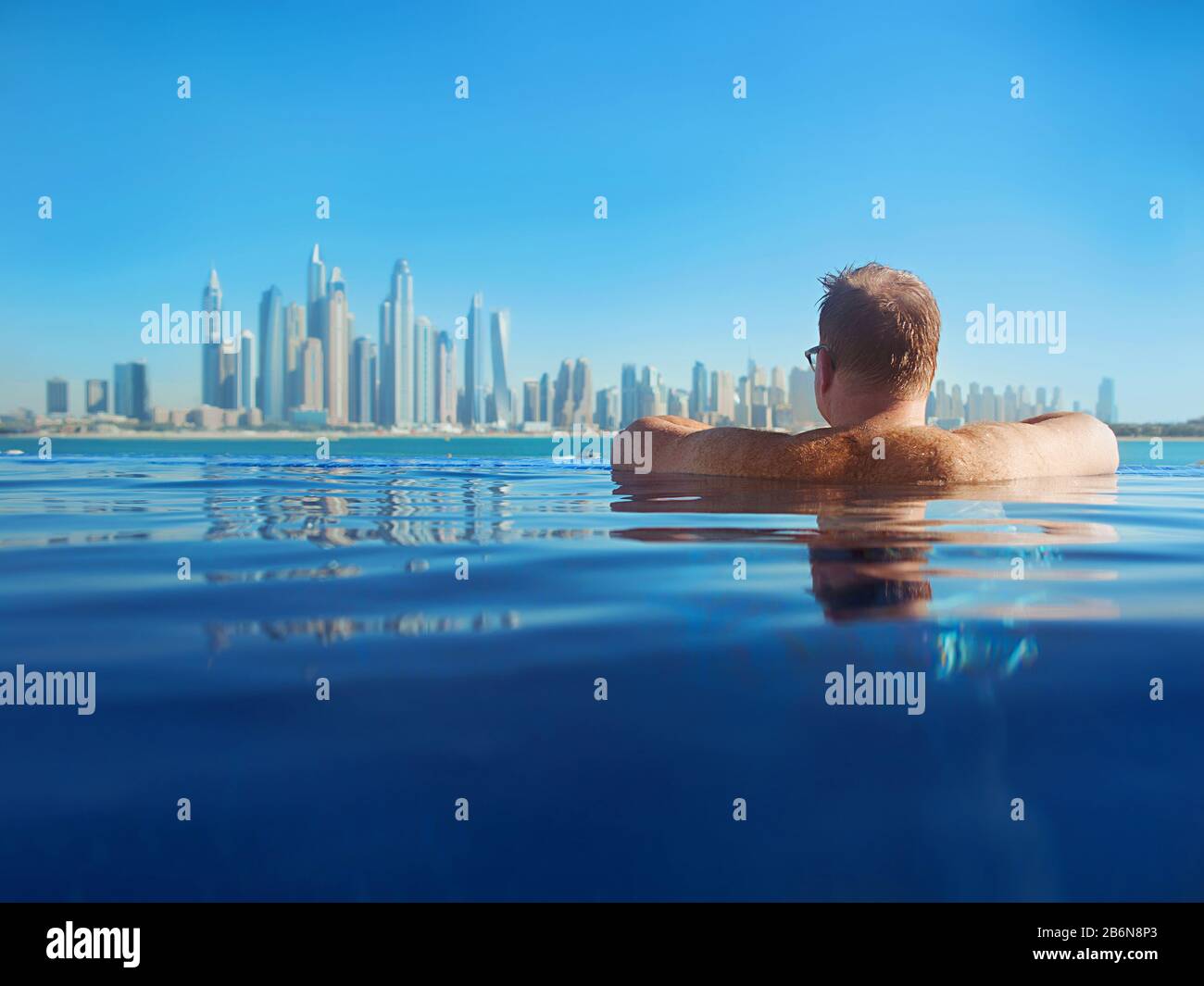 Porträt eines entspannten europäischen kaukasischen Rotkopfmannes mit Haaren zurück in Gläsern im Schwimmbad auf dem modernen Dubai (Vereinigte Arabische Emirate) und Meeresbac Stockfoto