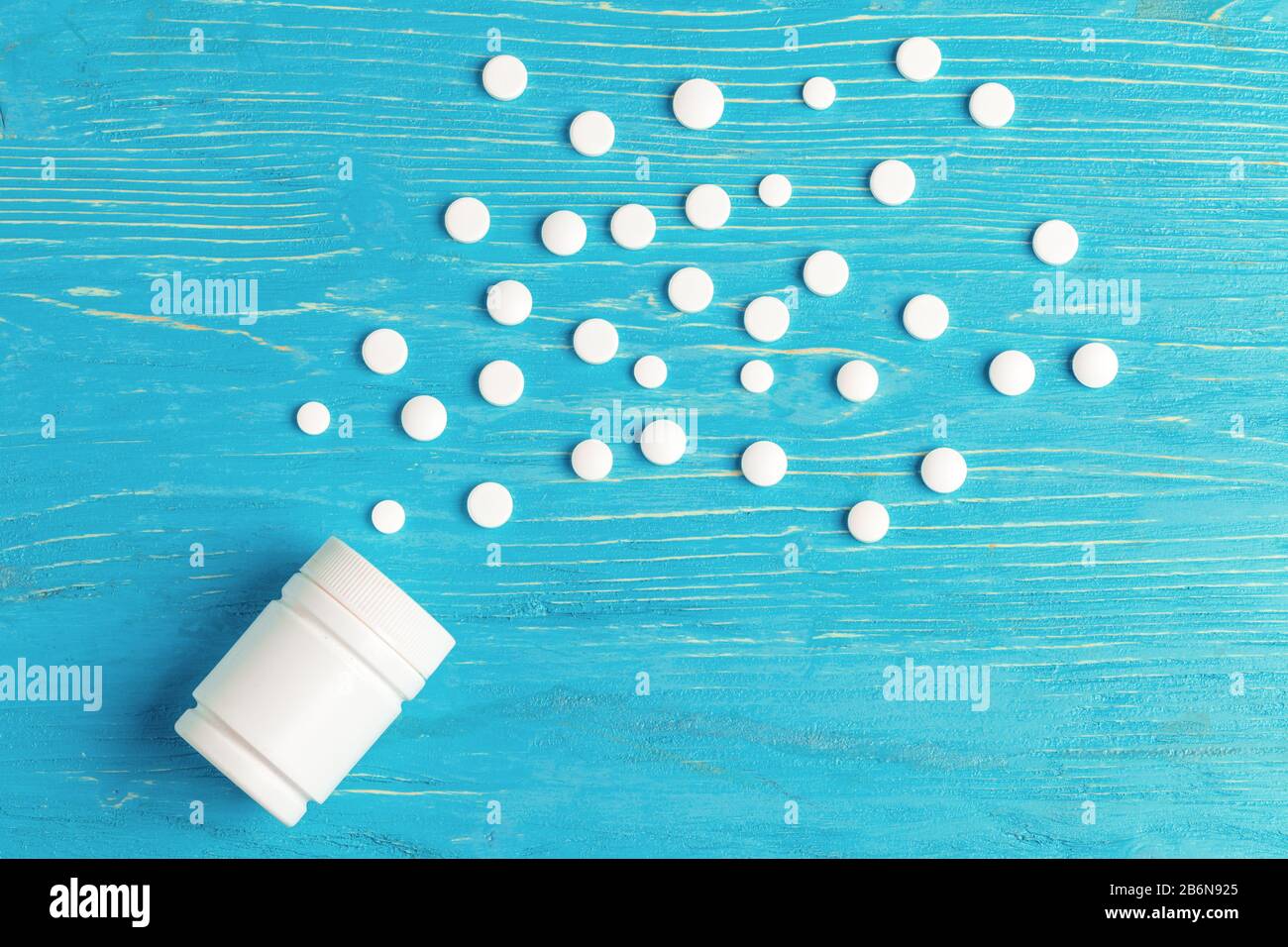Weiße Pillen wurden aus einem weißen Behälter über blauem Holzhintergrund verschüttet Stockfoto