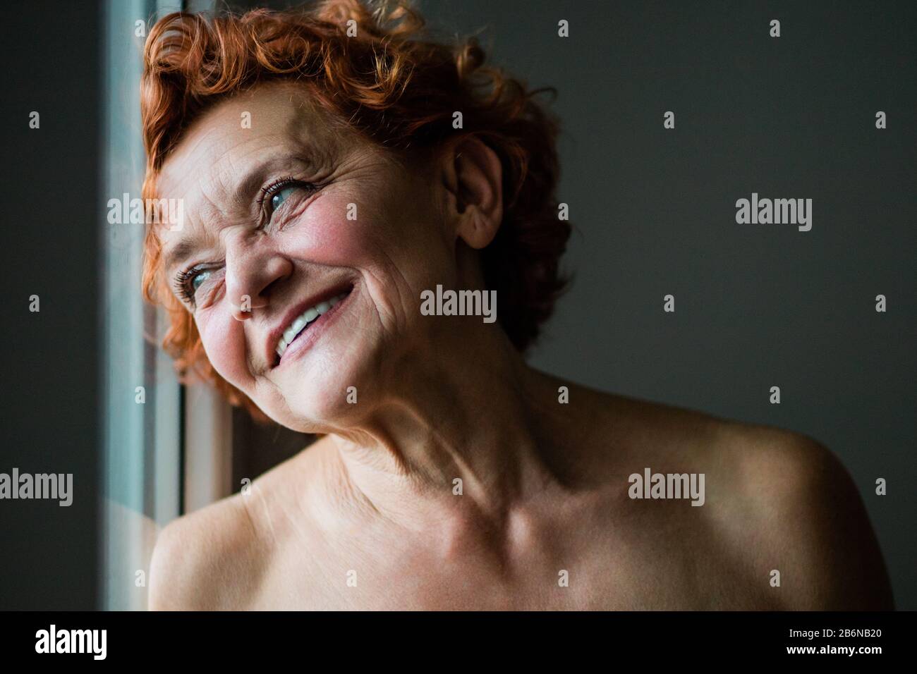 Fröhliche reife Frau lächelt am Fenster Stockfoto