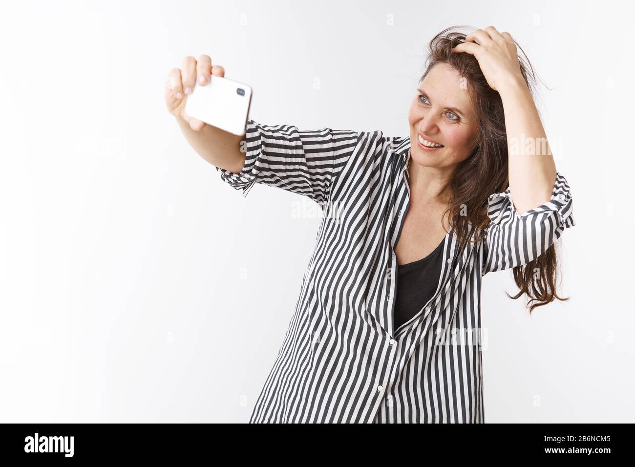 Noch jung und hübsch. Porträt einer charmanten selbstbewussten und unter Spannung stehenden Frau mittleren Alters, die Smartphone mit erweiterter Hand hält und selfie mitnimmt Stockfoto