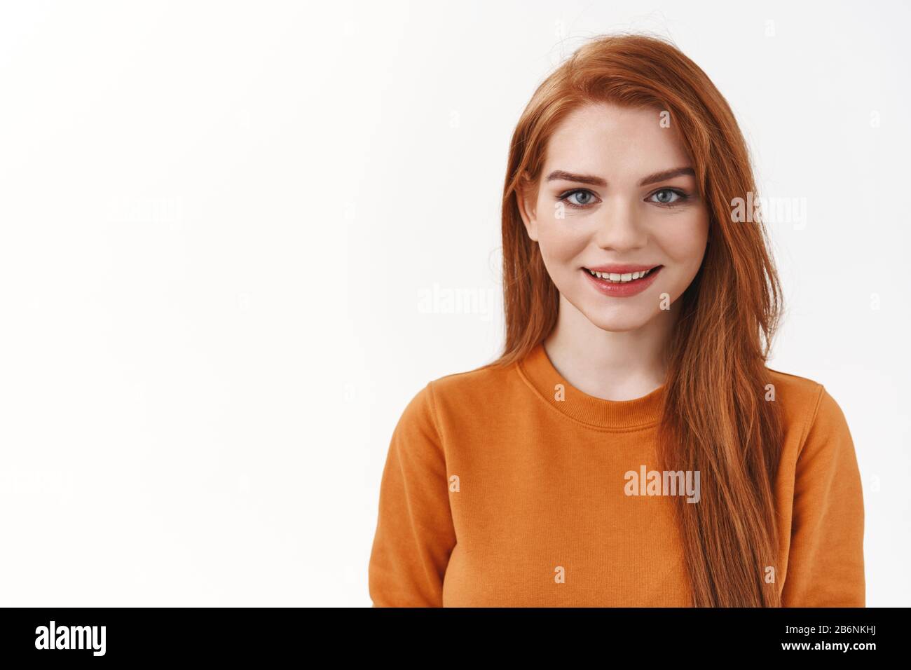 Nahaufnahme ziemlich charismatisches lächelndes Mädchen im orangefarbenen Pullover, sehen Kamera vertrauenswürdig aus mit niedlichem Grinsen, stehendem weißen Hintergrund fröhlich Stockfoto