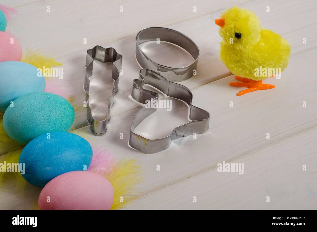 Osterbacken. Spielzeughuhn mit bunten Ostereiern und Plätzchenschneider auf weißem Holzhintergrund mit Kopierraum. Frohe ostern. Seitenansicht. Stockfoto