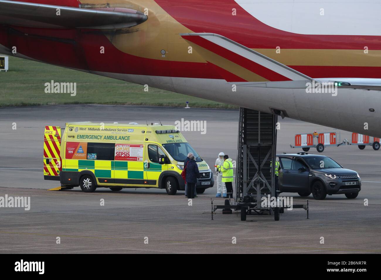 Ein Mitglied des NHS West Midlands Ambulance Service, das Schutzkleidung und eine Gesichtsmaske trägt, spricht mit den Passagieren (links) vom von Coronavirus geschlagenen Kreuzfahrtschiff Grand Princess, nachdem sie nach ihrer Rückführung aus den USA auf den Flughafen Birmingham angekommen sind. PA Foto. Bilddatum: Mittwoch, 11. März 2020. Rund 140 britische Urlauber waren vor der Westküste Amerikas auf dem Schiff gestrandet, nachdem 21 Menschen positiv auf das Virus an Bord getestet hatten. Siehe PA Story HEALTH Coronaviru. Der Lichtbildkredit sollte lauten: Steve Parsons/PA Wire Stockfoto