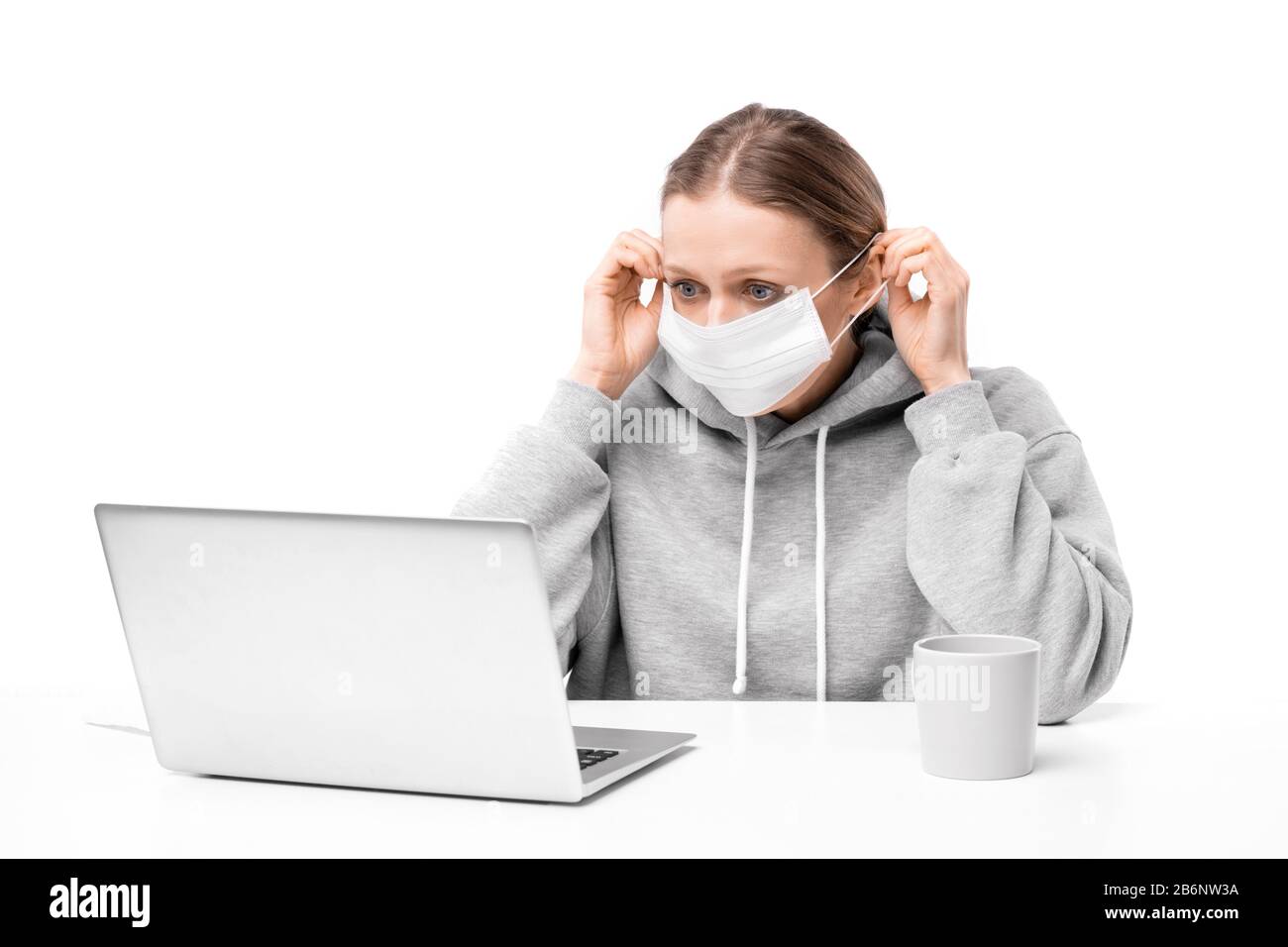 Junge Frau erschrocken mit Coronavirus Gesichtsmaske und Lesen von Nachrichten auf Laptop, weißer Hintergrund Stockfoto
