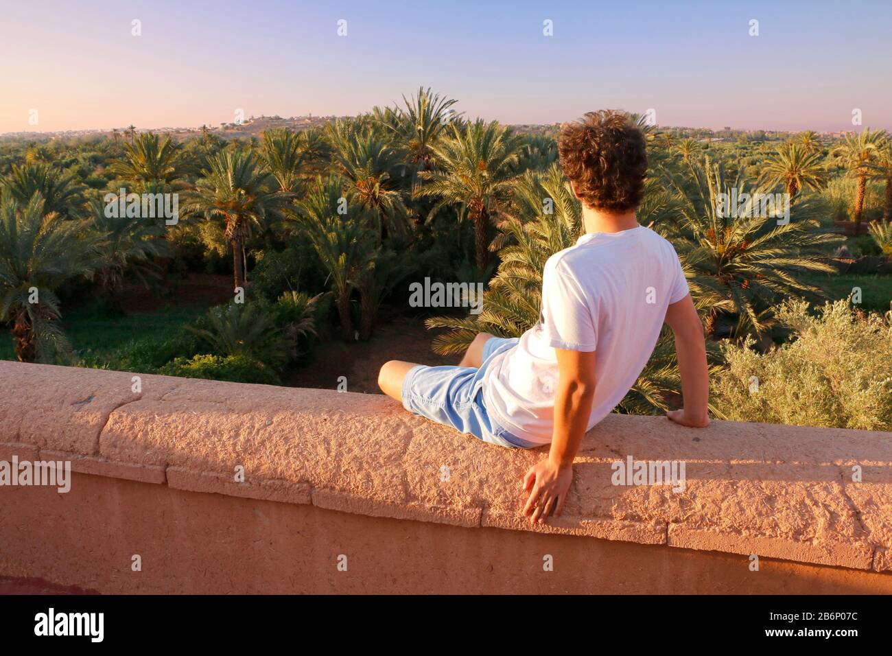 Marokkanische Wüste und Palmen mit jungem Modell, das auf einer Lehmwand sitzt Stockfoto