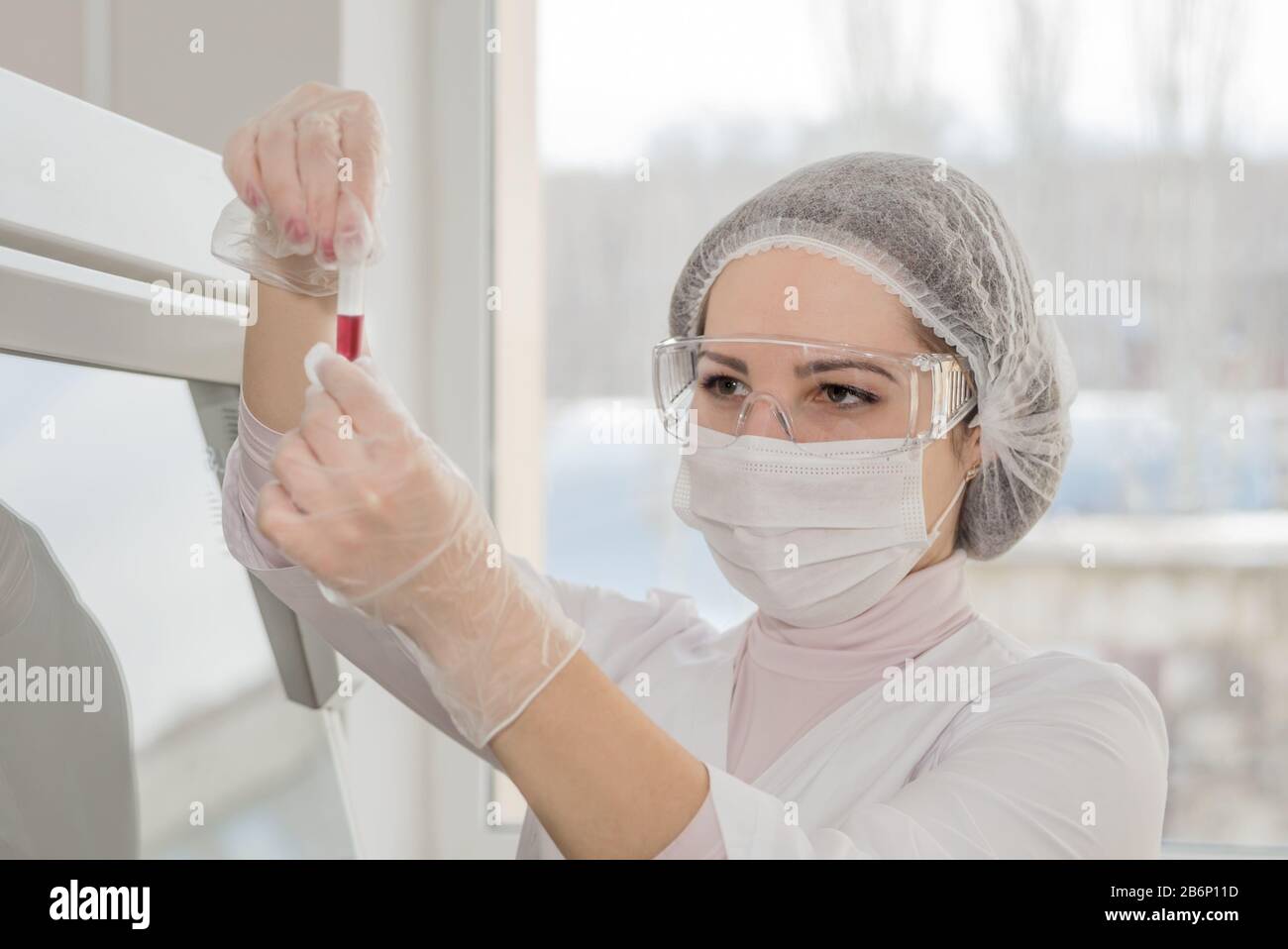Das Sanitäter einer Frau in einer weißen Schutzkleidung untersucht mit Blut in einem Reagenzglas in einem echten Labor Stockfoto