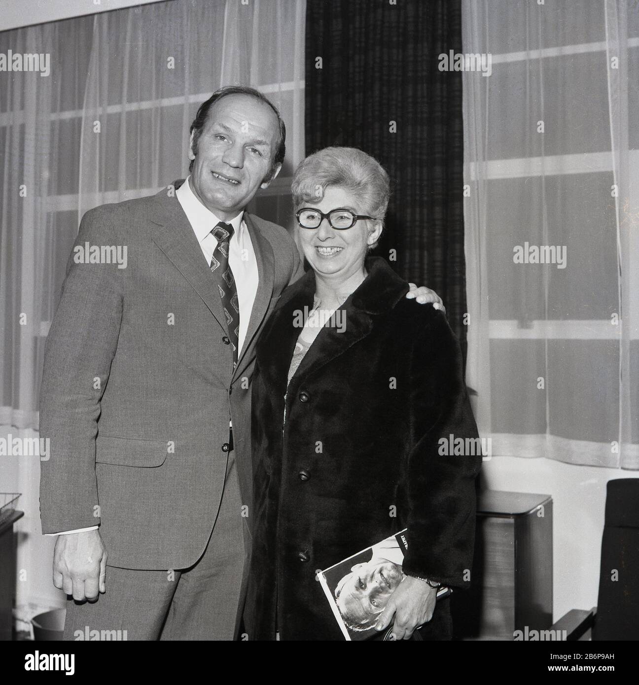 1972, der historische, Legendäre britische Schwergewichts-Boxmeister Henry Cooper, der für ein Bild mit einem lächelnden, glücklichen Fan steht, einer Dame in einem Fellmantel, die eine Kopie seiner Autobiografie hält, Catford, South East London, England, Großbritannien. Cooper war selbst eine sehr beliebte Sportpersönlichkeit, die in Lambeth geboren wurde und als einziger Boxer einen Ritterschlag erhielt. Stockfoto