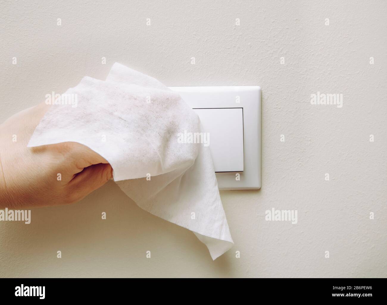 Nahaufnahme der Hand der Frau mit antibakteriellem Nasswischen zur Desinfektion des elektrischen Schalters am Hausraum an der Wand. Stockfoto