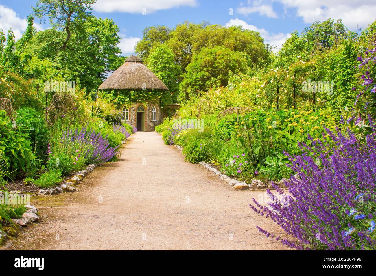 Das 19. Jahrhundert strohgedeckten runden Haus, umgeben von schönen Blumenbeeten und Schotterwege, das in der ummauerten Garten in West Dean Gärten in West Sussex Stockfoto