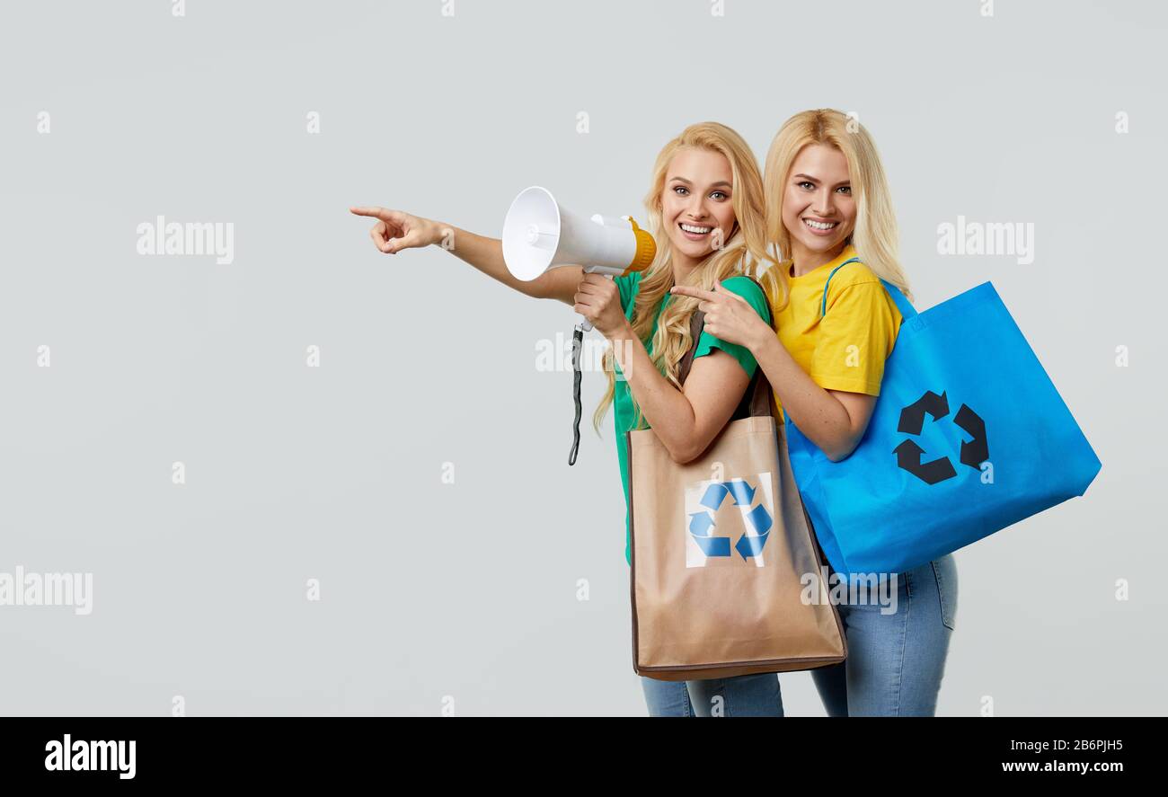 Junge Frauen in legeren Kleidungsstücken halten ökologische recycelte Lebensmittellaschen und schreien in ein Megafon, um Plastikmüll zu recyceln. Zeigen Sie links auf leer Stockfoto