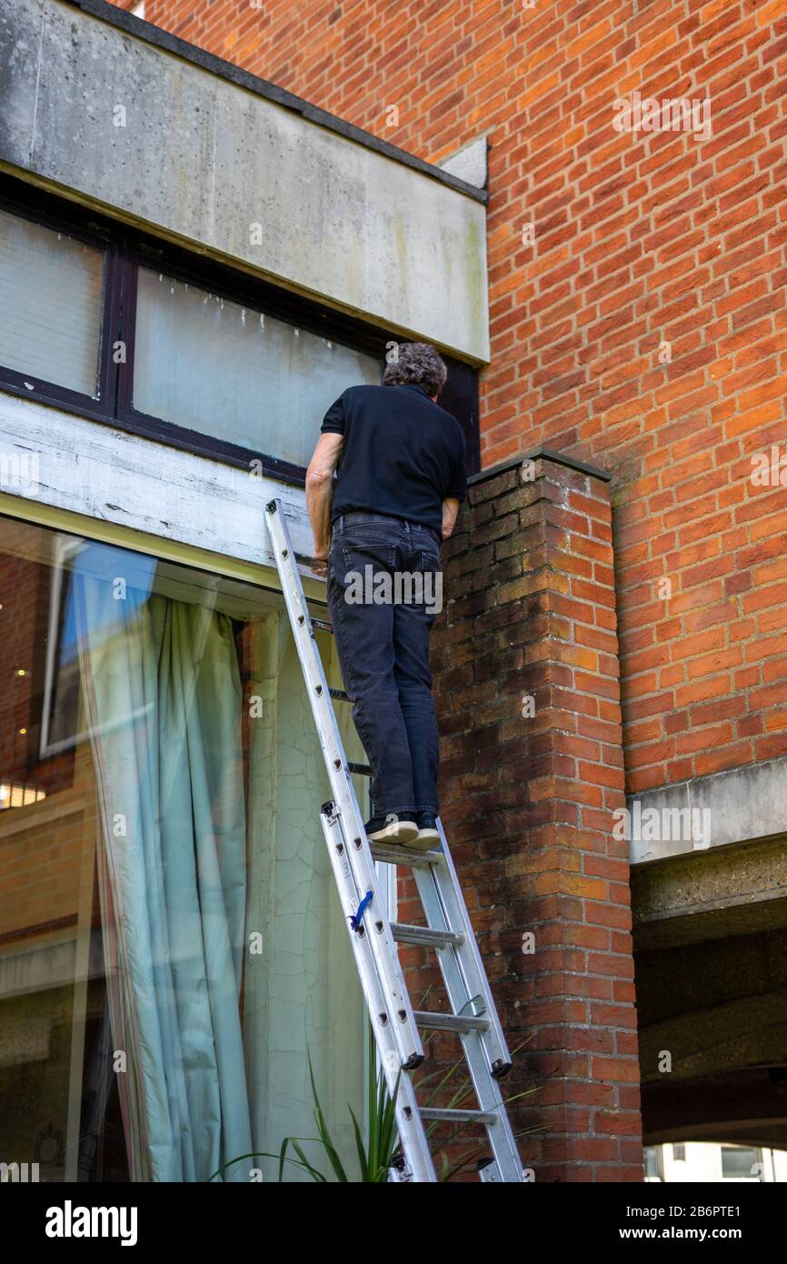 Ein Erbauer, der eine Leiter erklimmt, um Reparaturarbeiten durchzuführen Stockfoto