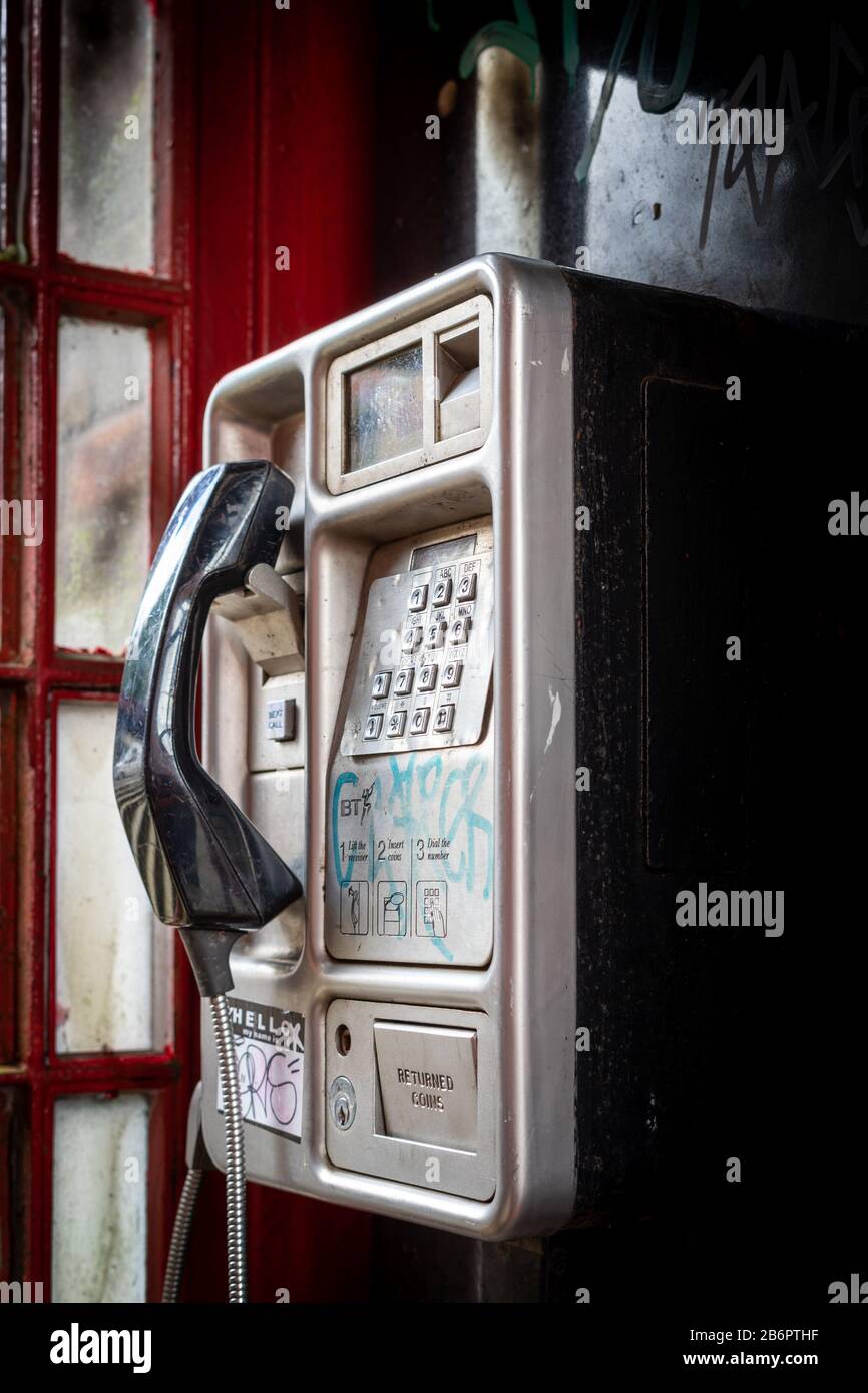 Ein altes Münztelefon in einer roten Telefonbox das Wurde verwüstet Stockfoto