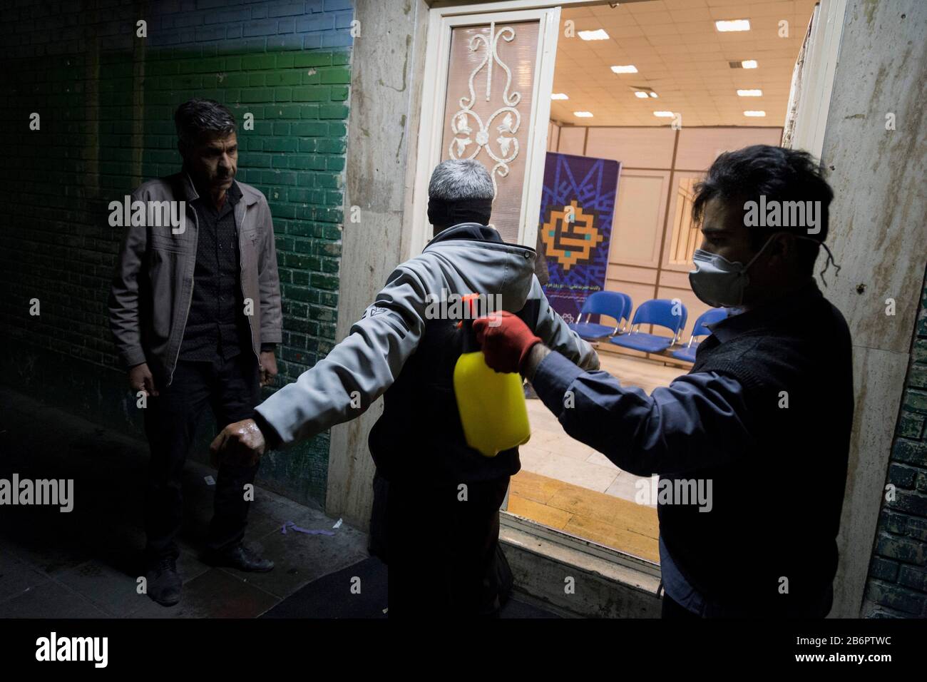 Teheran, Iran. März 2020. Ein Mitarbeiter im Schutzraum sprüht Desinfektionsmittel zur Desinfektion von Obdachlosen, bevor er nach einem neuen Coronavirus (Covid-19) im Iran in Khavaran Obdachlose Shelter im Süden Teherans eindringt. Die Khavaran-Halle soll 600 Personen beherbergen. Diese Kapazität wird in der Winternacht auf 1.100 ausgedehnt. In der Anlage sind auch Saisonarbeiter untergebracht, die duschen, eine warme Mahlzeit pro Tag essen und dort schlafen. Kredit: Zuma Press, Inc./Alamy Live News Stockfoto