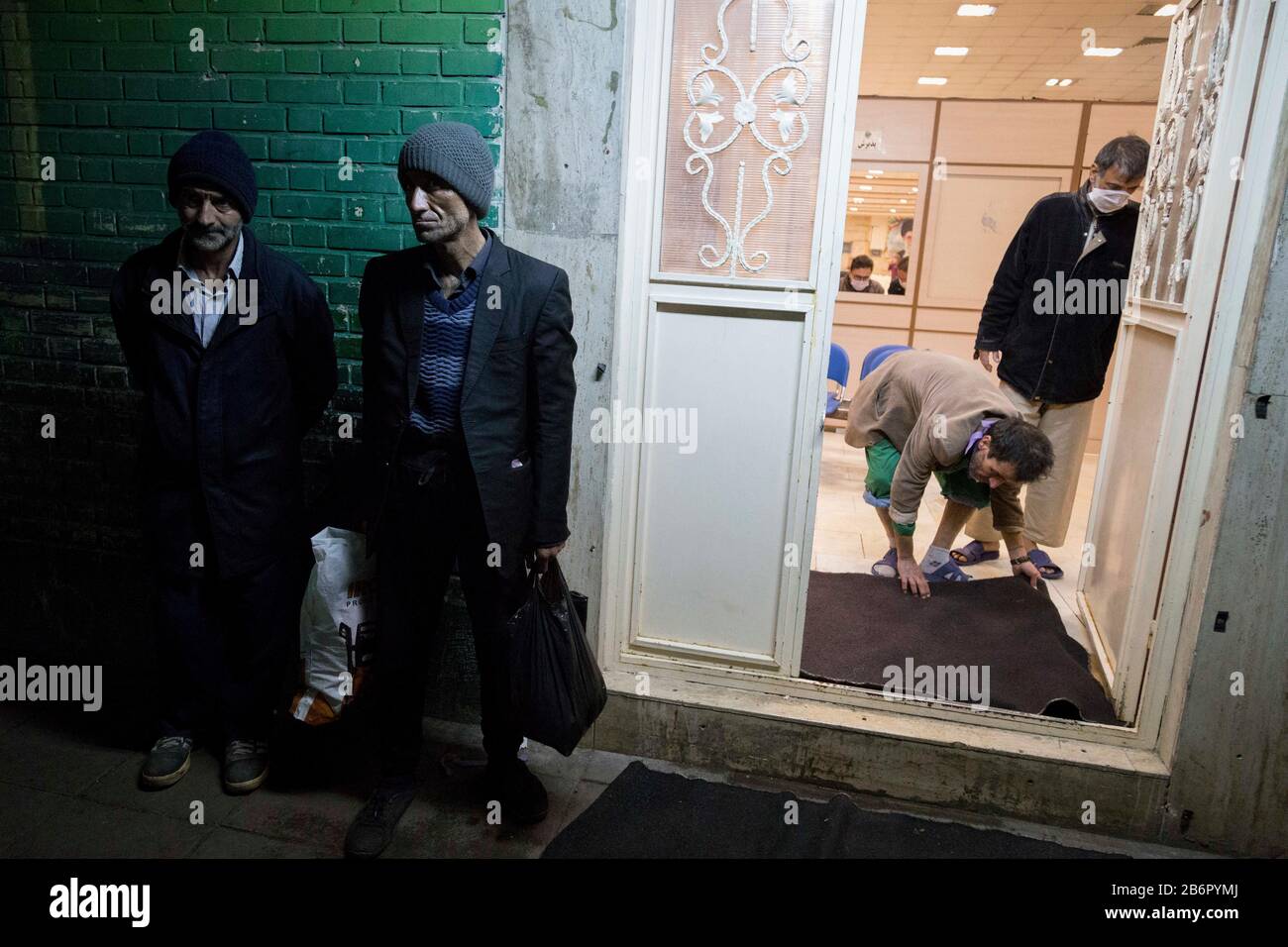 Teheran, Iran. März 2020. Obdachlose Männer stehen auf, während sie warten, von einem Mitarbeiter zu desinfizieren, bevor sie nach einem neuen Coronavirus (Covid-19)-Ausbruch im Iran in Khavaran Obdachlose Shelter im Süden Teherans eindringen. Die Khavaran-Halle soll 600 Personen beherbergen. Diese Kapazität wird in der Winternacht auf 1.100 ausgedehnt. In der Anlage sind auch Saisonarbeiter untergebracht, die duschen, eine warme Mahlzeit pro Tag essen und dort schlafen. Kredit: Zuma Press, Inc./Alamy Live News Stockfoto