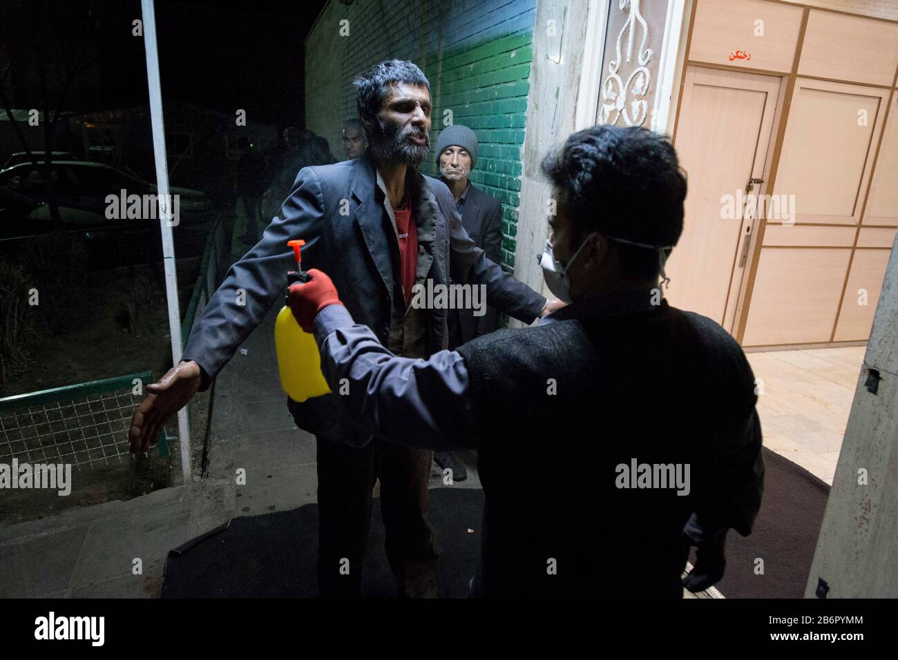 Teheran, Iran. März 2020. Ein Mitarbeiter im Schutzraum sprüht Desinfektionsmittel zur Desinfektion von Obdachlosen, bevor er nach einem neuen Coronavirus (Covid-19) im Iran in Khavaran Obdachlose Shelter im Süden Teherans eindringt. Die Khavaran-Halle soll 600 Personen beherbergen. Diese Kapazität wird in der Winternacht auf 1.100 ausgedehnt. In der Anlage sind auch Saisonarbeiter untergebracht, die duschen, eine warme Mahlzeit pro Tag essen und dort schlafen. Kredit: Zuma Press, Inc./Alamy Live News Stockfoto