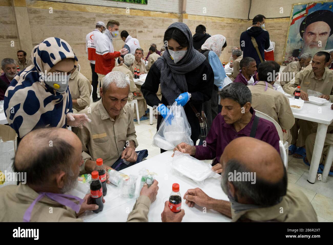 Teheran, Iran. März 2020. Eine freiwillige Frau gibt Obdachlosen in Khavaran Obdachlosen im Süden Teherans nach einem neuen Coronavirus (Covid-19)-Ausbruch im Iran Lebensmittelpakete. Die Khavaran-Halle soll 600 Personen beherbergen. Diese Kapazität wird in der Winternacht auf 1.100 ausgedehnt. In der Anlage sind auch Saisonarbeiter untergebracht, die duschen, eine warme Mahlzeit pro Tag essen und dort schlafen. Kredit: Zuma Press, Inc./Alamy Live News Stockfoto