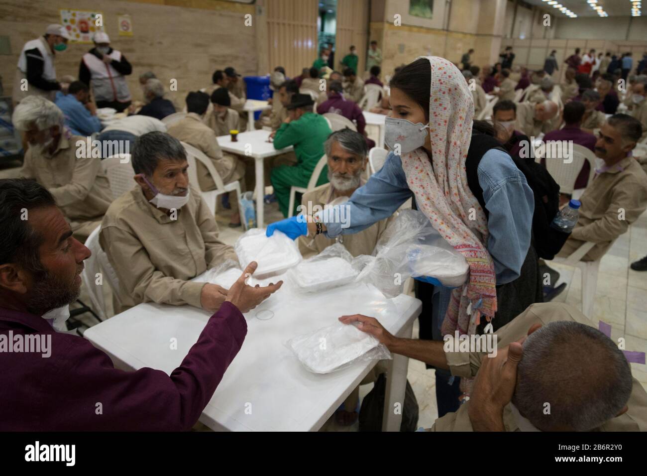 Teheran, Iran. März 2020. Eine freiwillige Frau gibt Obdachlosen in Khavaran Obdachlosen im Süden Teherans nach einem neuen Coronavirus (Covid-19)-Ausbruch im Iran Lebensmittelpakete. Die Khavaran-Halle soll 600 Personen beherbergen. Diese Kapazität wird in der Winternacht auf 1.100 ausgedehnt. In der Anlage sind auch Saisonarbeiter untergebracht, die duschen, eine warme Mahlzeit pro Tag essen und dort schlafen. Kredit: Zuma Press, Inc./Alamy Live News Stockfoto