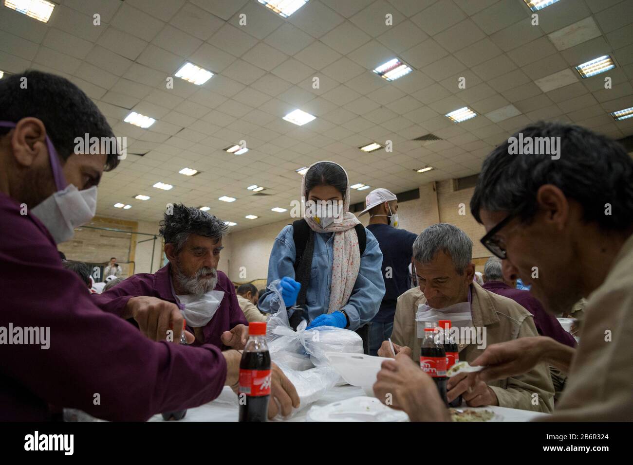 Teheran, Iran. März 2020. Eine freiwillige Frau gibt Obdachlosen in Khavaran Obdachlosen im Süden Teherans nach einem neuen Coronavirus (Covid-19)-Ausbruch im Iran Lebensmittelpakete. Die Khavaran-Halle soll 600 Personen beherbergen. Diese Kapazität wird in der Winternacht auf 1.100 ausgedehnt. In der Anlage sind auch Saisonarbeiter untergebracht, die duschen, eine warme Mahlzeit pro Tag essen und dort schlafen. Kredit: Zuma Press, Inc./Alamy Live News Stockfoto