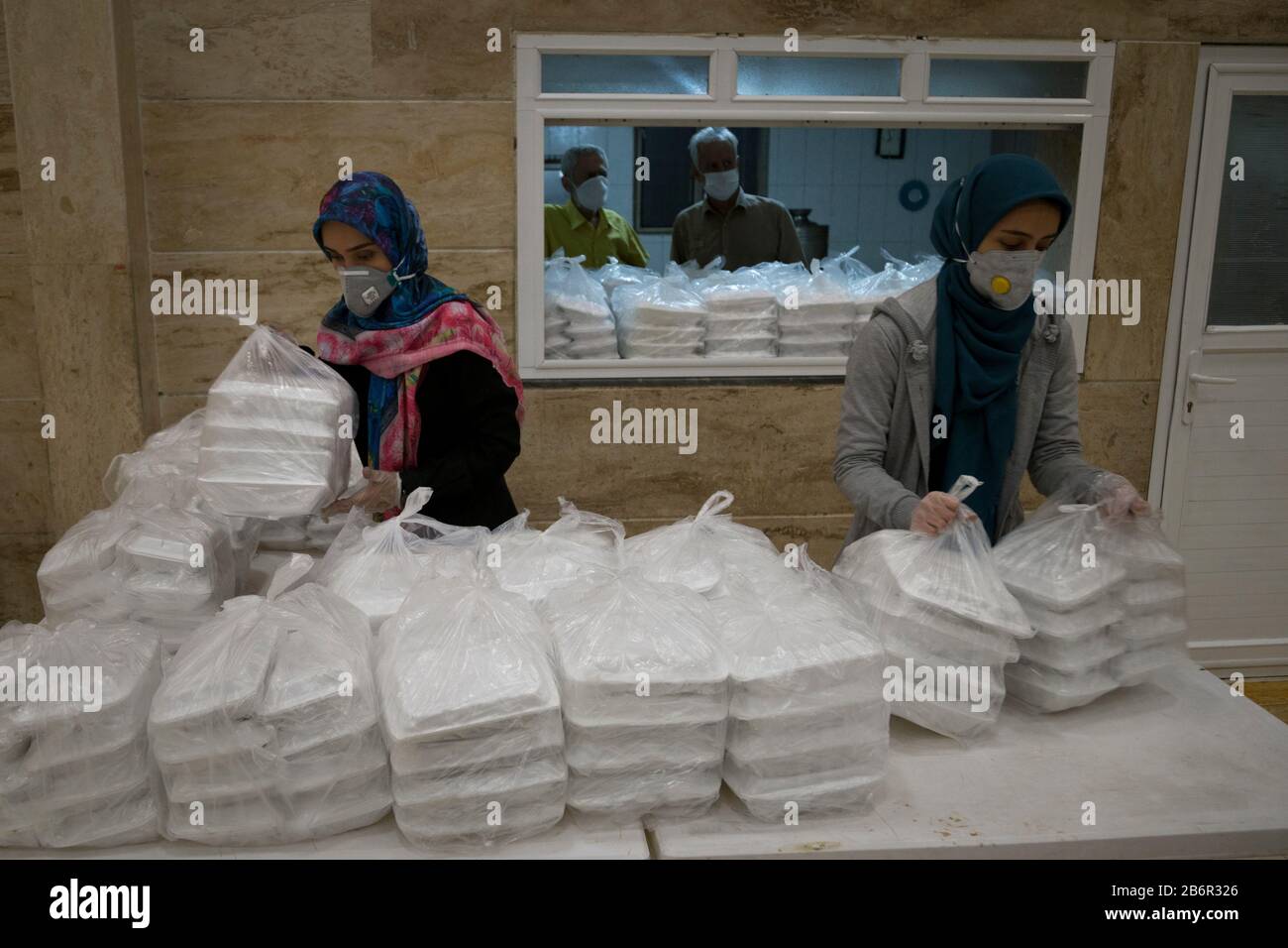 Teheran, Iran. März 2020. Freiwillige Frauen bereiten Lebensmittelpackungen für obdachlose Männer vor, im Obdachlosenheim Khavaran im Süden Teherans nach einem neuen Ausbruch des Coronavirus (Covid-19) im Iran. Die Khavaran-Halle soll 600 Personen beherbergen. Diese Kapazität wird in der Winternacht auf 1.100 ausgedehnt. In der Anlage sind auch Saisonarbeiter untergebracht, die duschen, eine warme Mahlzeit pro Tag essen und dort schlafen. Kredit: Zuma Press, Inc./Alamy Live News Stockfoto