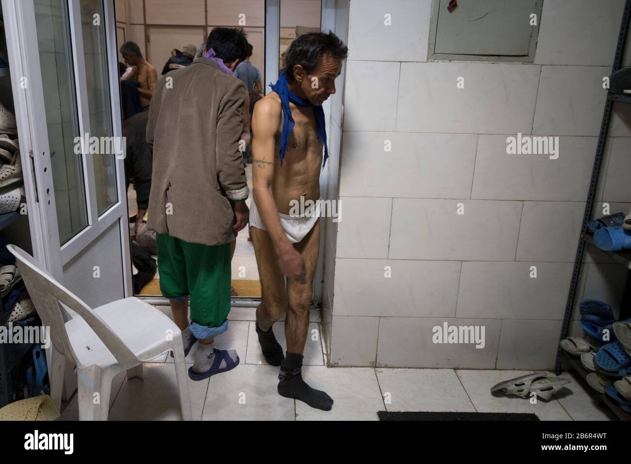 Teheran, Iran. März 2020. Obdachlose Männer entfernen ihre Kleidung, nachdem sie nach einem neuen Ausbruch des Coronavirus (Covid-19) im Iran in Khavaran Obdachlose Shelter im Süden Teherans desinfiziert haben. Die Khavaran-Halle soll 600 Personen beherbergen. Diese Kapazität wird in der Winternacht auf 1.100 ausgedehnt. In der Anlage sind auch Saisonarbeiter untergebracht, die duschen, eine warme Mahlzeit pro Tag essen und dort schlafen. Kredit: Zuma Press, Inc./Alamy Live News Stockfoto