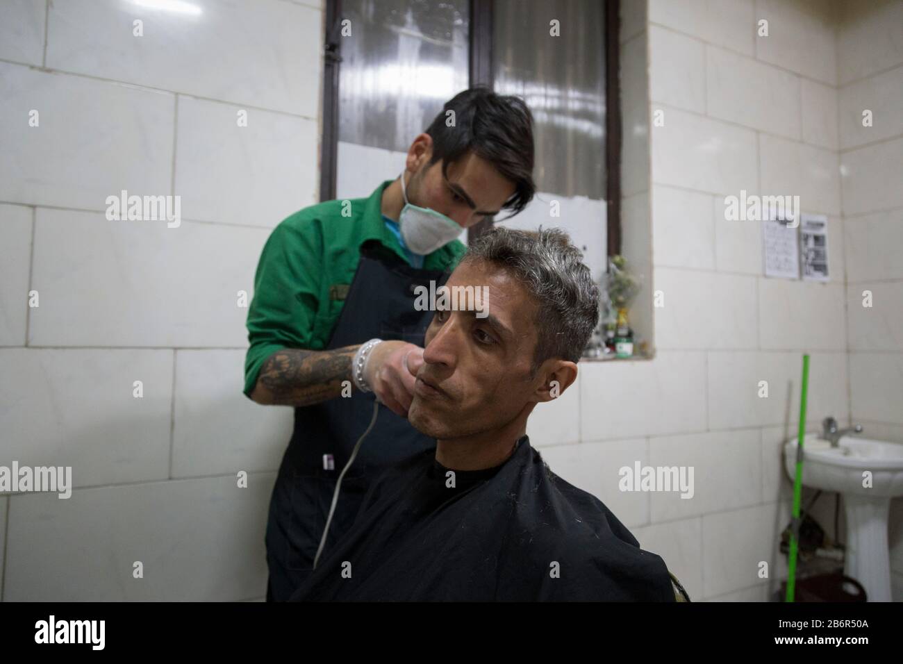 Teheran, Iran. März 2020. Ein Mitarbeiter Schneidet einem Obdachlosen in Khavaran Obdachlosen Obdachlosenheim im Süden Teherans nach einem neuen Coronavirus (Covid-19) Ausbruch im Iran die Haare. Die Khavaran-Halle soll 600 Personen beherbergen. Diese Kapazität wird in der Winternacht auf 1.100 ausgedehnt. In der Anlage sind auch Saisonarbeiter untergebracht, die duschen, eine warme Mahlzeit pro Tag essen und dort schlafen. Kredit: Zuma Press, Inc./Alamy Live News Stockfoto
