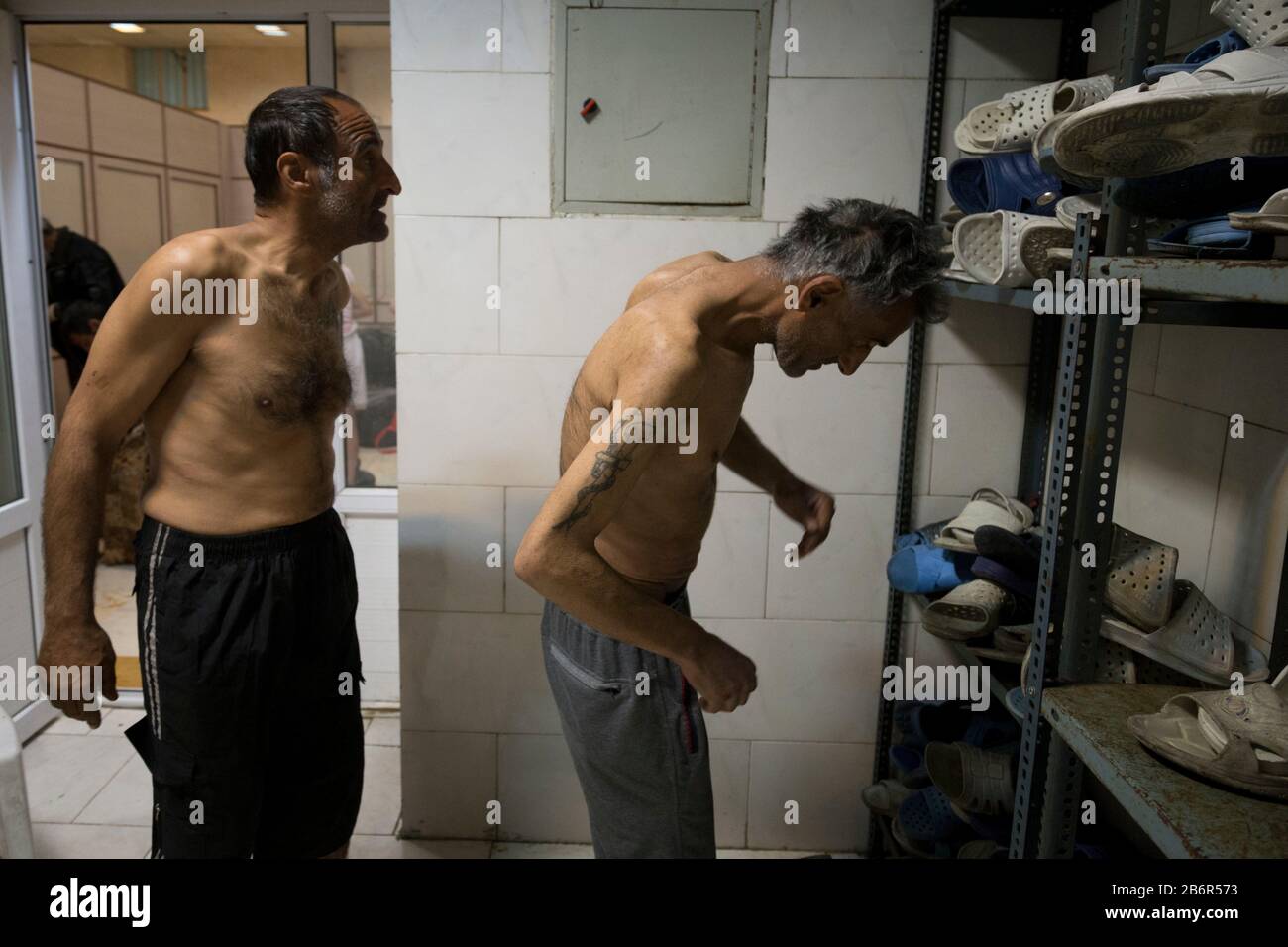 Teheran, Iran. März 2020. Obdachlose Männer entfernen ihre Kleidung, nachdem sie nach einem neuen Ausbruch des Coronavirus (Covid-19) im Iran in Khavaran Obdachlose Shelter im Süden Teherans desinfiziert haben. Die Khavaran-Halle soll 600 Personen beherbergen. Diese Kapazität wird in der Winternacht auf 1.100 ausgedehnt. In der Anlage sind auch Saisonarbeiter untergebracht, die duschen, eine warme Mahlzeit pro Tag essen und dort schlafen. Kredit: Zuma Press, Inc./Alamy Live News Stockfoto