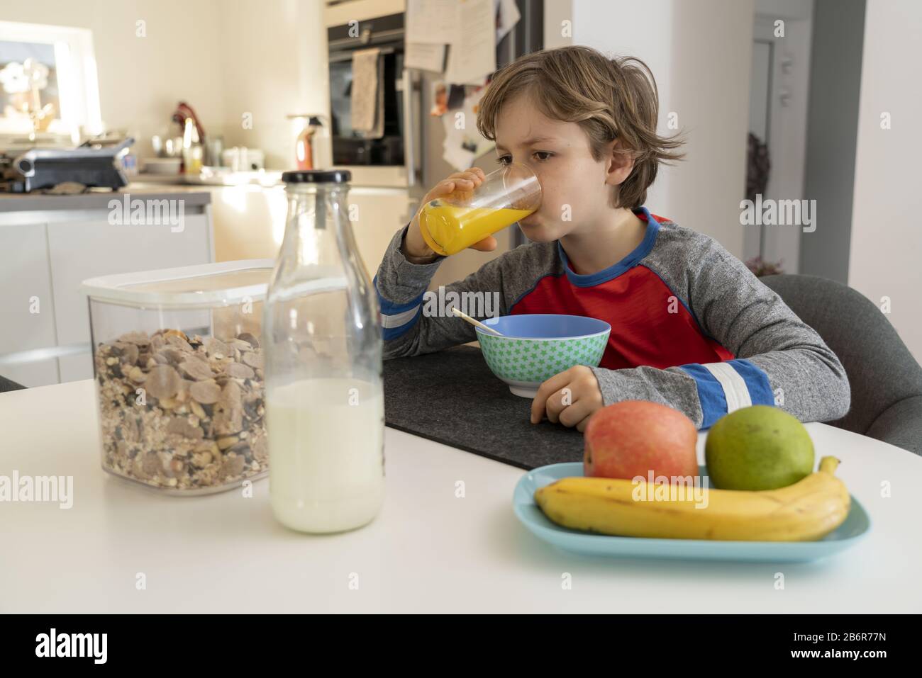 Jung, 9 Jahre alt, zum Frühstück, zu Hause, vor der Schule, gesundes Frühstück, mit Milch, Orangensaft, Obst, Müsli, Stockfoto