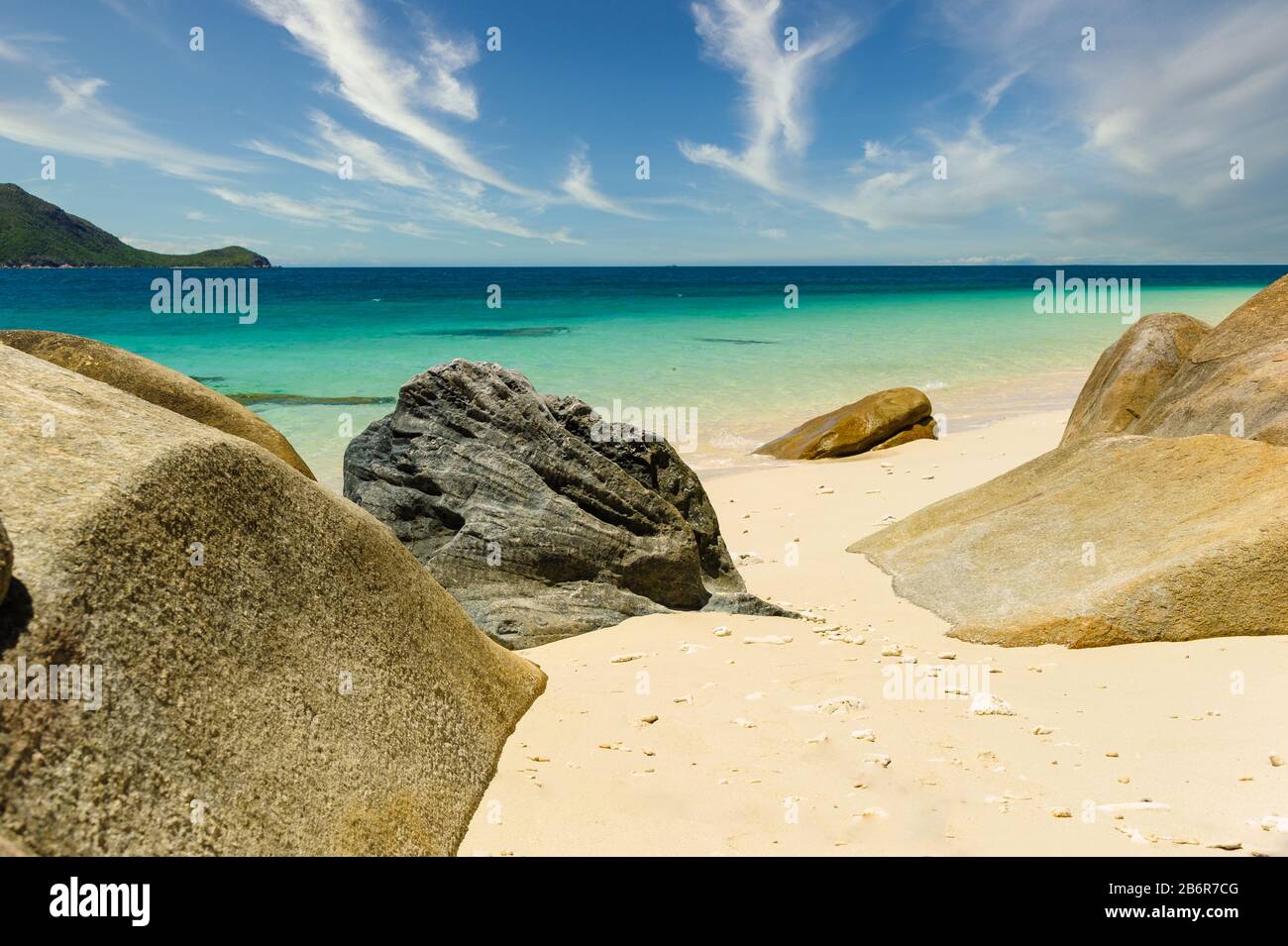 Blick über blaugrünes, kristallklares Wasser des Pazifischen Ozeans von der Ufervegetation Nudey Beach, die mit runden Strandbrocken durchsetzt ist. Stockfoto
