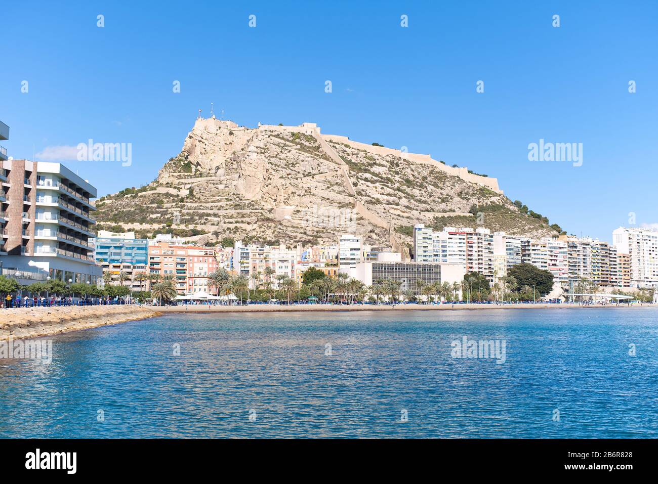 Blick auf die Burg Santa Barbara am Berg Benacantil vom Strand an der Küste von Alicante am Mittelmeer an einem sonnigen Tag in hellblau. Stockfoto