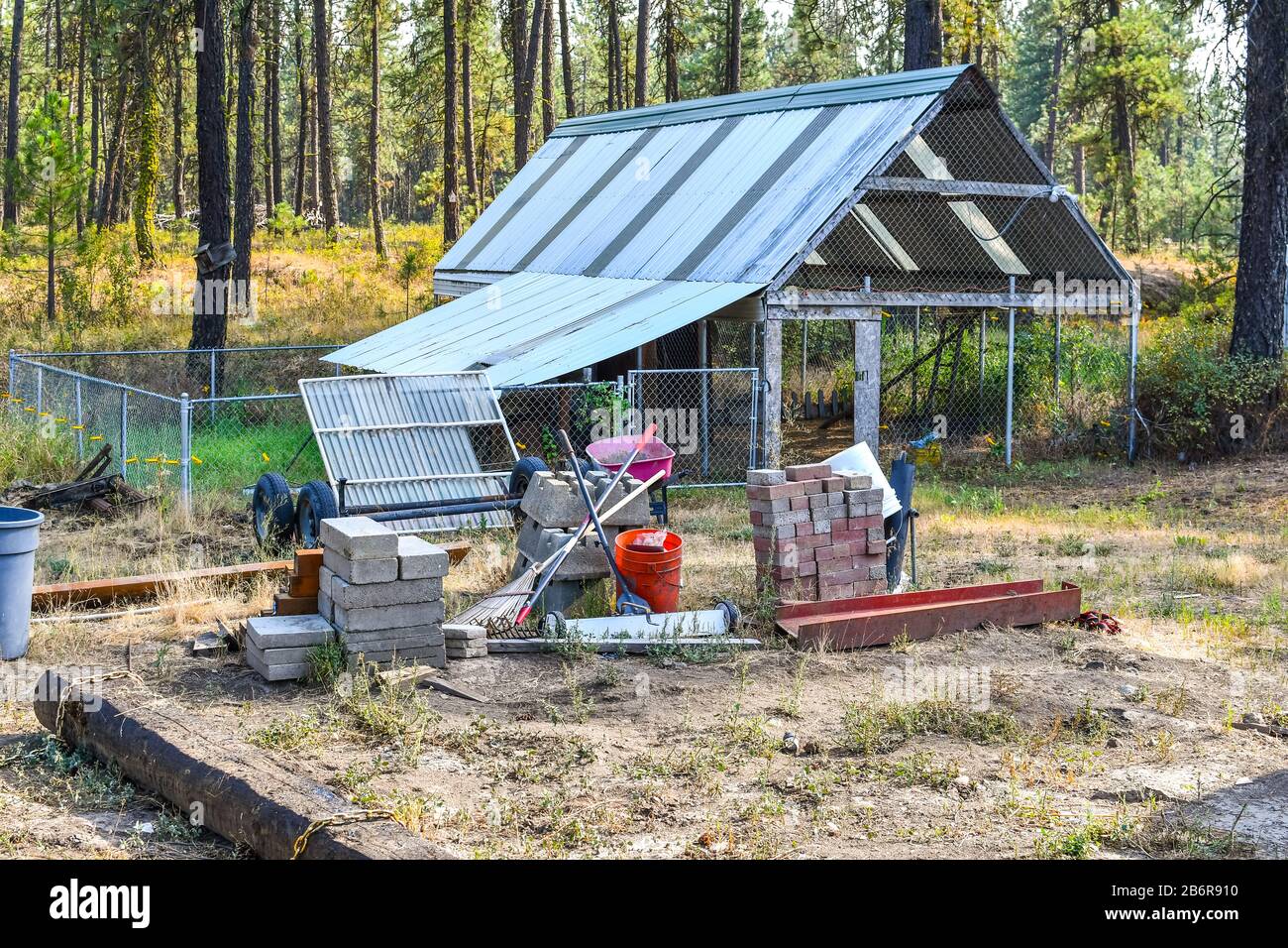 Werkzeuge für Garten- und Baustoffe sitzen auf einem Schmutzplatz mit einem dahinter liegenden Gewächshaus in ländlicher Umgebung. Stockfoto