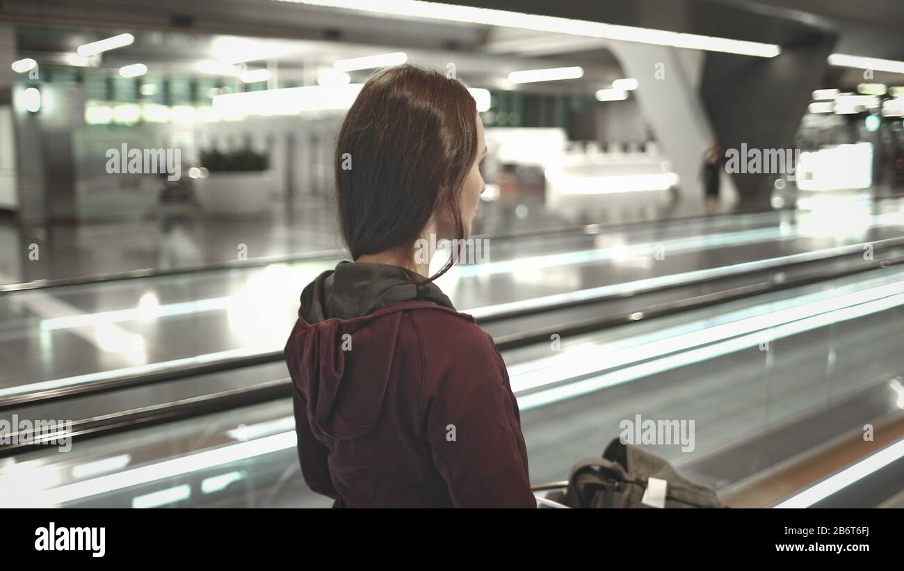 Junges Mädchen mit Gepäck Spaziergang auf Flughafen Speedwalk. Seitenansicht der Frau Bewegen Sie sich zum Boarding Gate. Transitpassagierin, Reisender auf Travelator. Modernes Internationales Terminal. Stockfoto