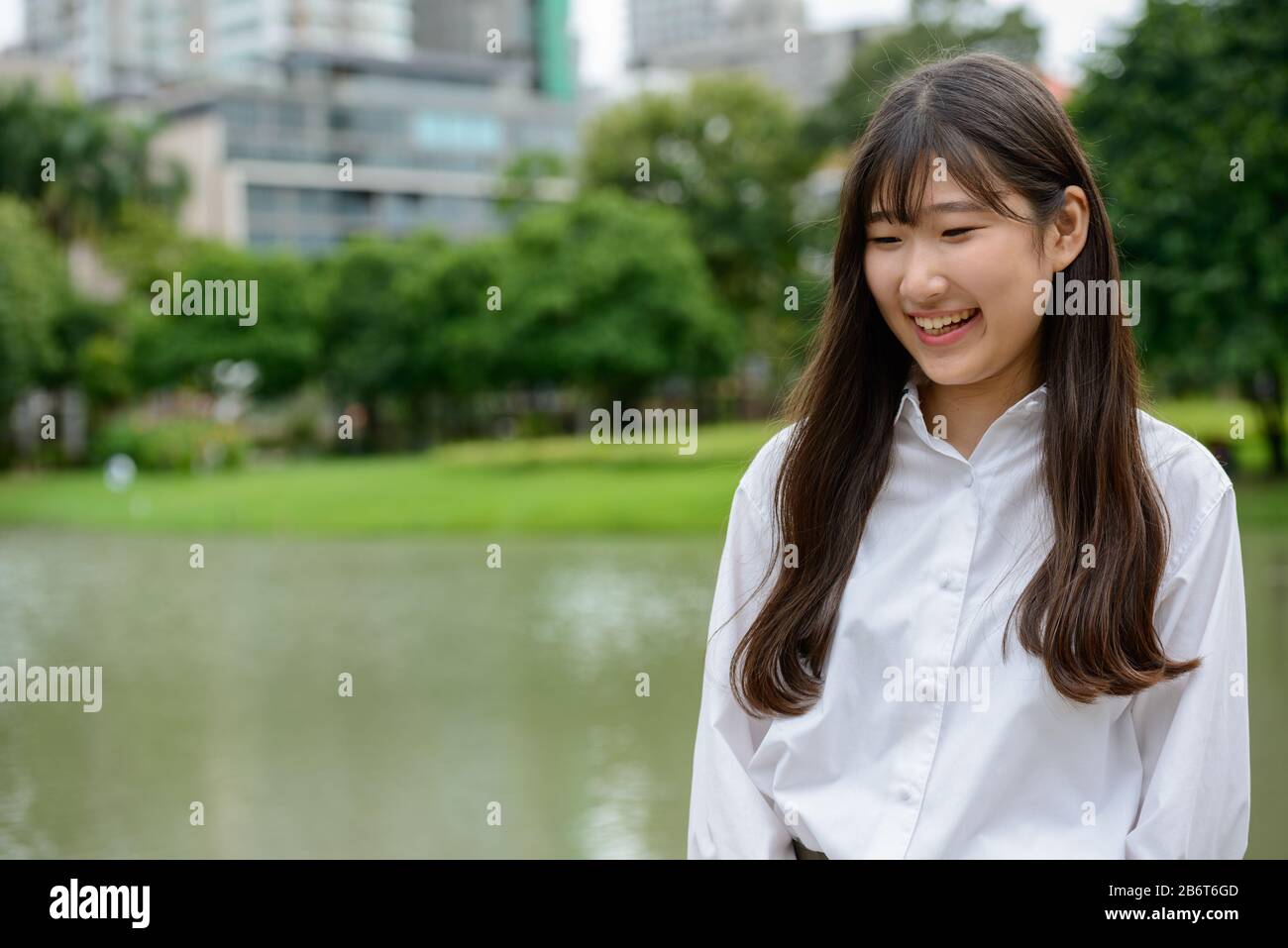 Fröhliches junges, wunderschönes asiatisches Teenager-Mädchen, das im Park denkt Stockfoto