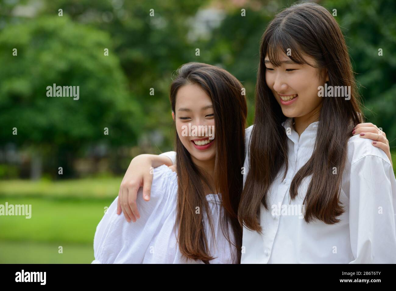 Zwei glückliche junge, schöne asiatische Teenager-Mädchen, die sich im Park vereinigen Stockfoto