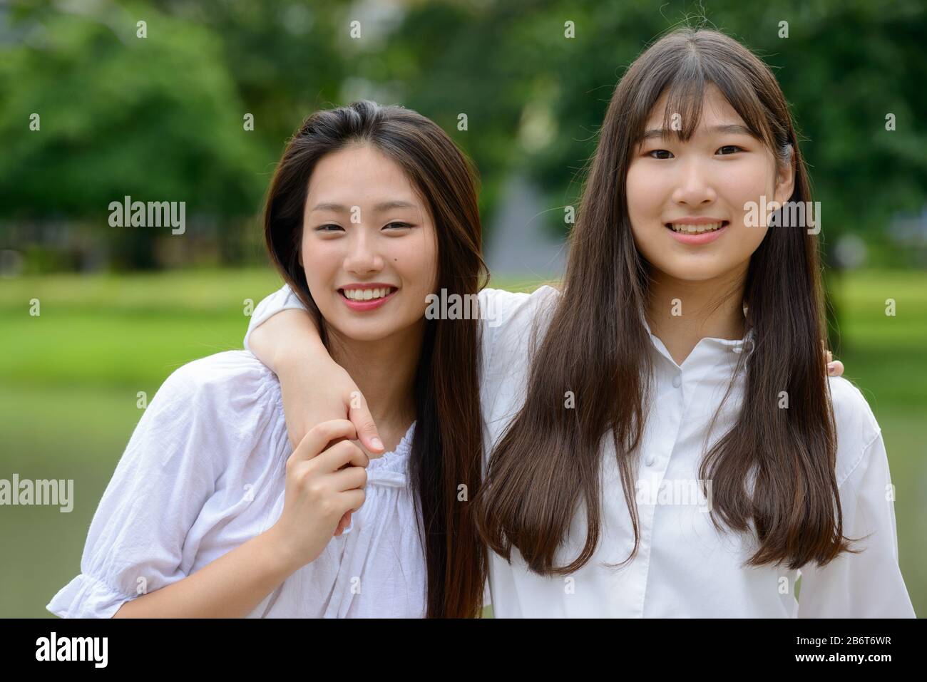 Zwei glückliche junge, schöne asiatische Teenager-Mädchen, die sich im Park vereinigen Stockfoto