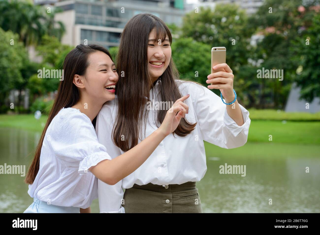 Zwei glückliche junge, schöne asiatische Teenager-Mädchen, die selfie im Park zusammen nehmen Stockfoto