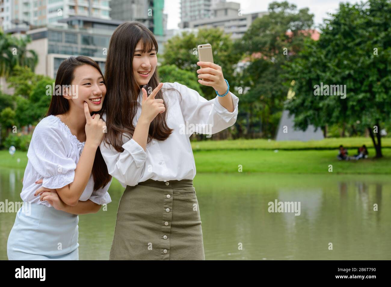 Zwei glückliche junge, schöne asiatische Teenager-Mädchen, die selfie im Park zusammen nehmen Stockfoto