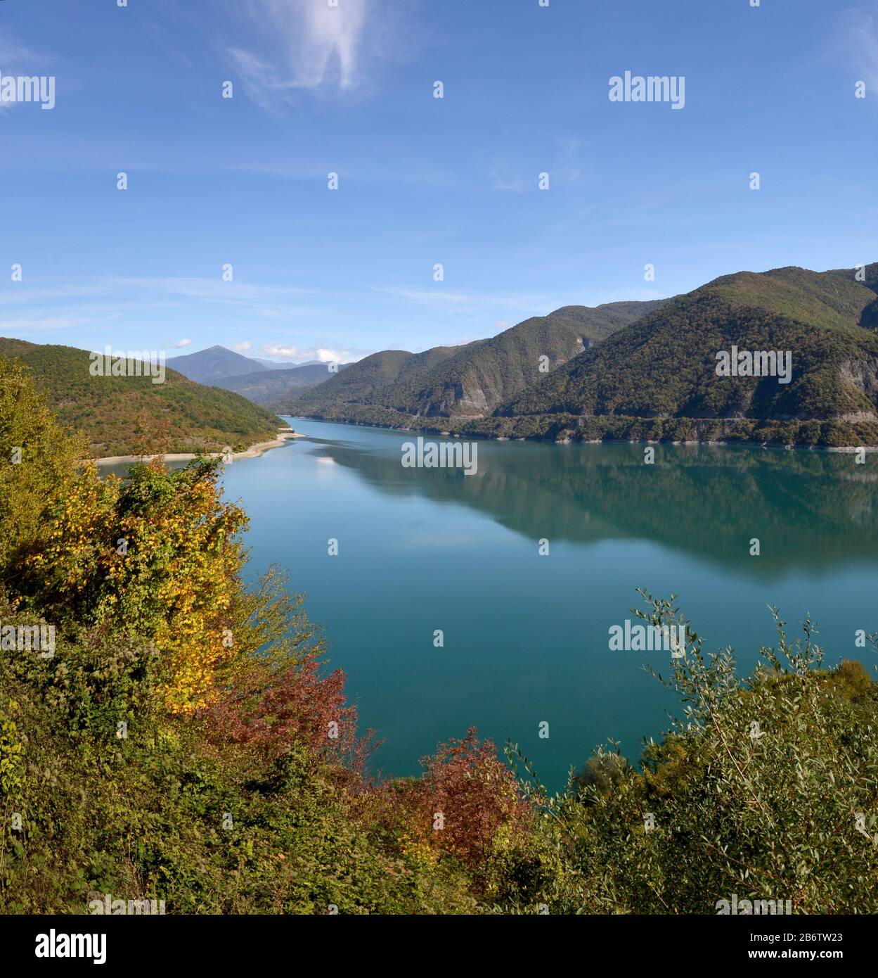 Der Azursee Ananuri ist umgeben von Herbstbäumen. Berge und Himmel spiegeln sich in ruhigem, glasig bewässertem Wasser wider. Stockfoto