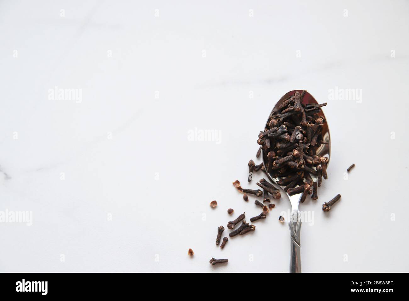 Getrocknete Nelken im Löffel auf grauem Marmorhintergrund. Gewürze für heißen Tee, Wintergetränke und Speisen. Nahaufnahme und Draufsicht Stockfoto