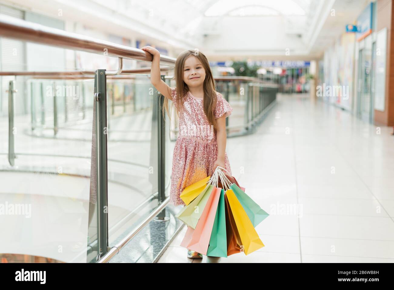 Hübsches lächelndes kleines Mädchen mit Einkaufstaschen im Laden. Schöne süße Momente der kleinen Prinzessin, ziemlich freundliches Kind, das Spaß an der Kamera hat. Stockfoto