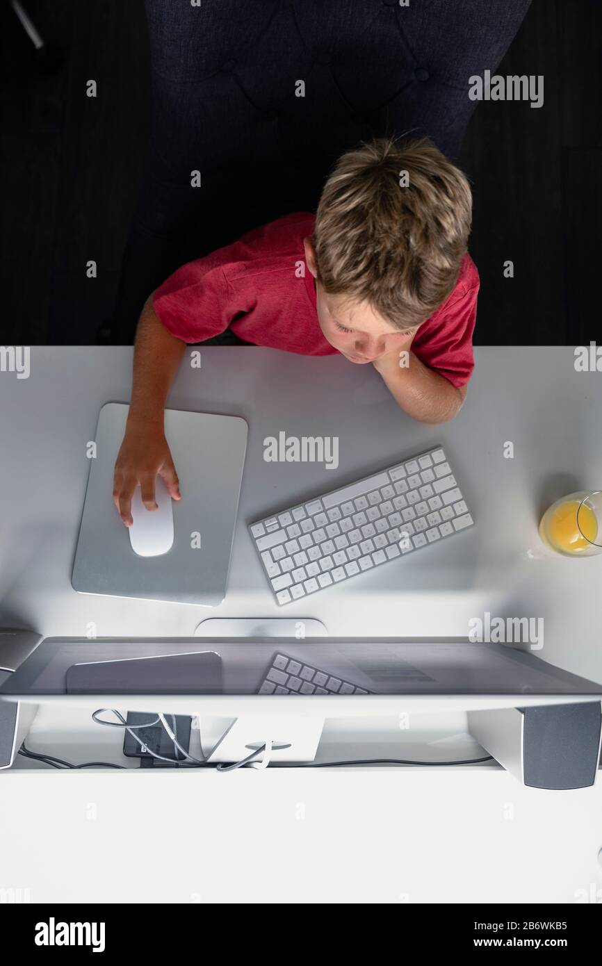 Ein direkt über dem Schuss sitzender junger Junge mit einem Computer zu Hause am Schreibtisch macht er Hausaufgaben. Stockfoto