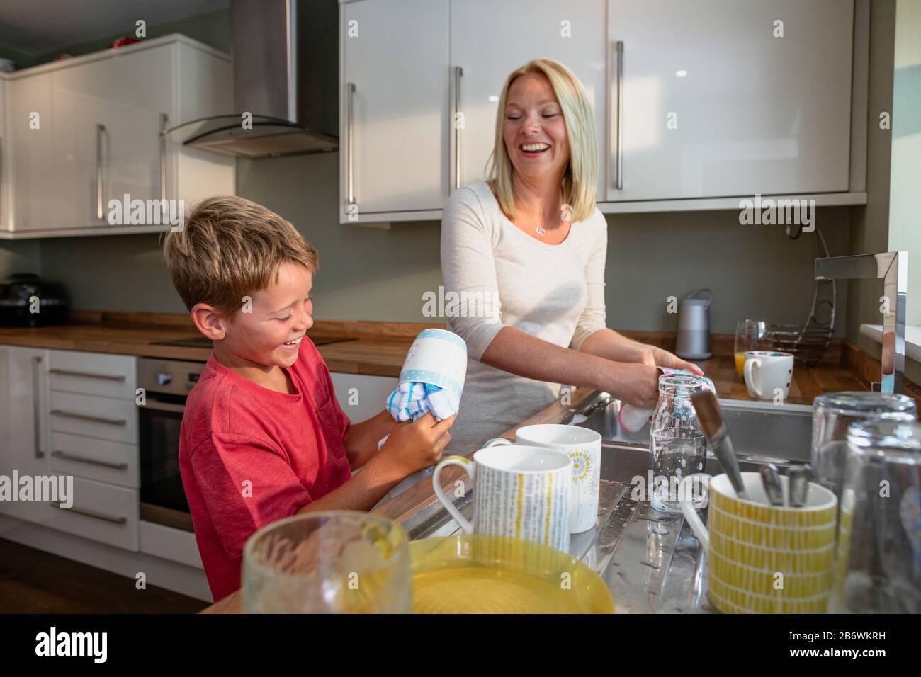 Ein seitlicher Schuss von einem kleinen Jungen und einer Mutter, die die Gerichte zusammen waschen. Stockfoto