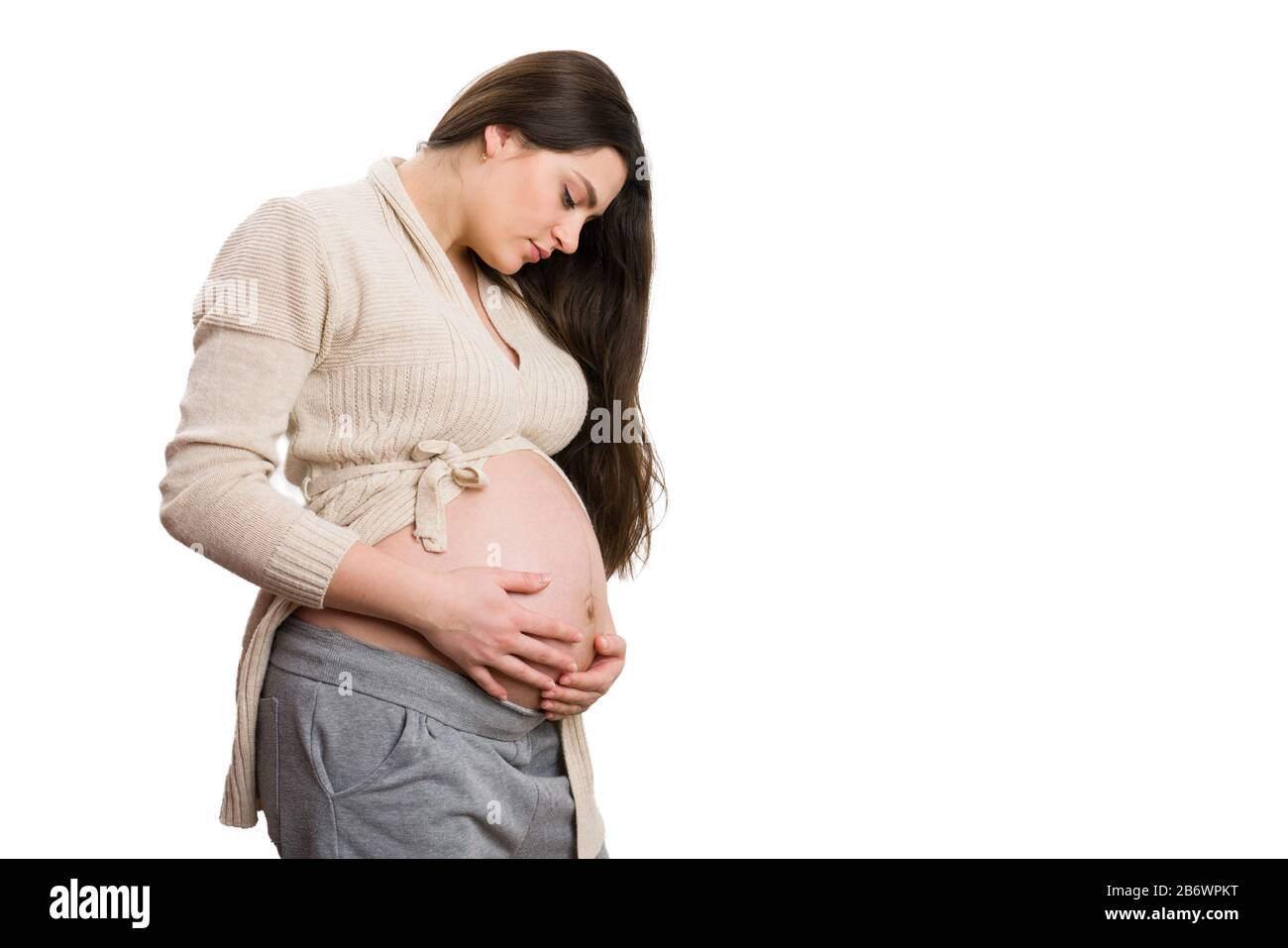 Schöne junge schwangere Frau, die ihren großen Bauch auf weißem Hintergrund als acht Monate Schwangerschaftskonzept überprüft Stockfoto