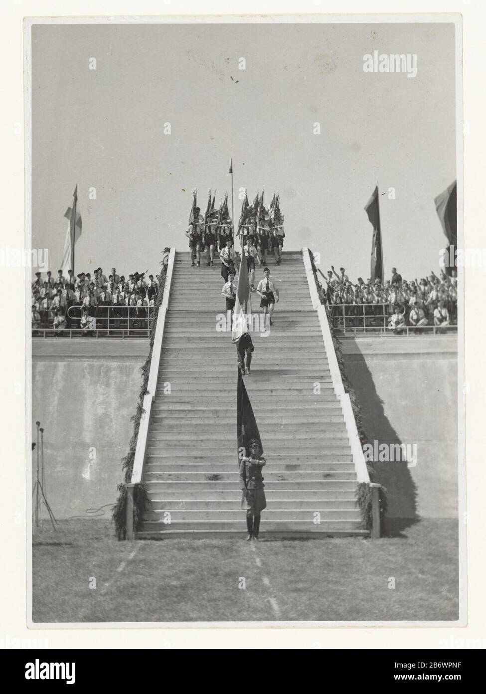 Jeugdstorm im Stadion Galgenwaard Jeugdstorm (serietitel) EINE lange Reihe von Mitgliedern des Jugendsturms, die am 20. Juni 1942 die Treppe im Galgenwaard-Stadion in Utrechter hinunterkommen. Im Stadion nehmen sie an der Einweihung von 3.000 Führungskräften des NSB Teil. Die Treppe hinab ist ein Wehrmachtssoldat mit einer Fahne. Auf den Tribünen sind links und rechts der Bühne Mitglieder des Jugendsturms. Einige bringen NSB-Grußwort: Gerader Arm wie der Hitlergruß und rufen: Hurray. Die Eidesfeier war das Ergebnis eines Kompromisses zwischen den Deutschen und dem NSB. Die Deutschen wollten einen Eid auf Hitler (den Mussert Stockfoto