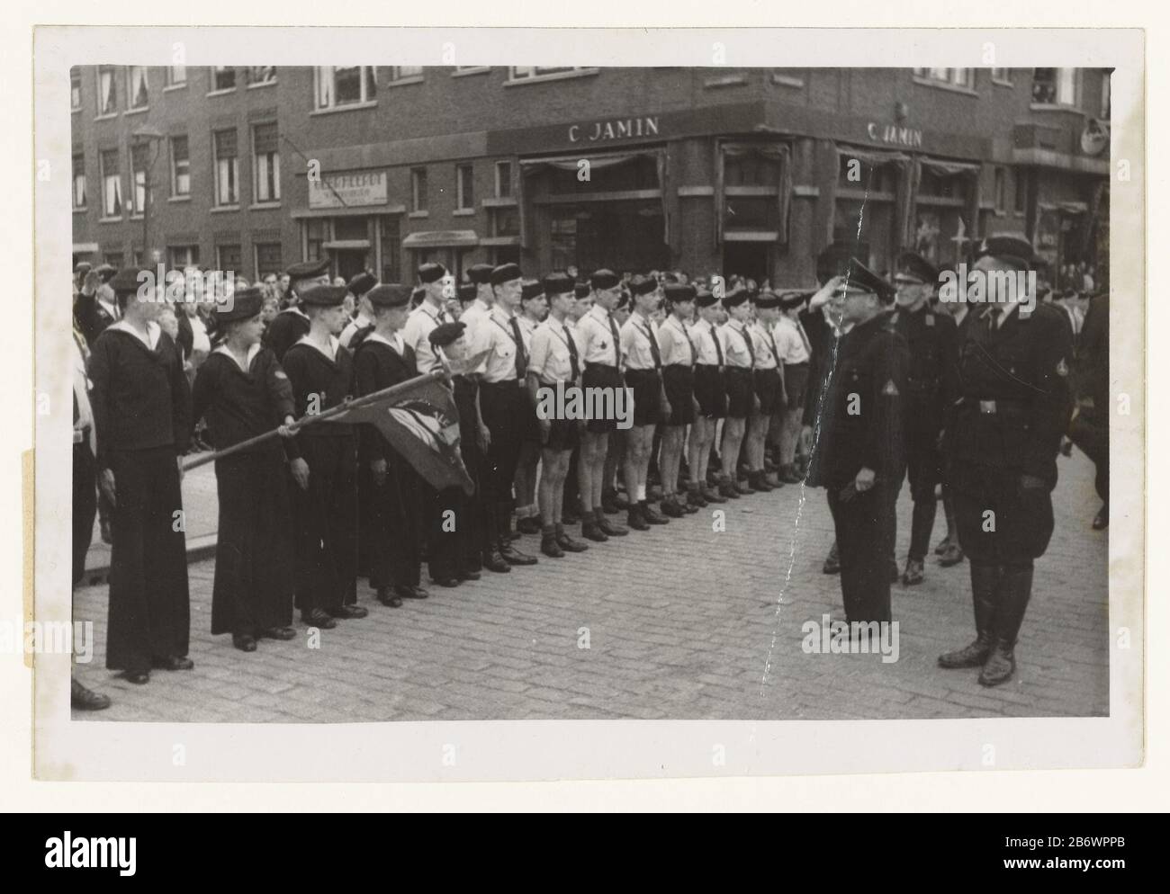 Jeugdstorm begroet Mussert Jeugdstorm (serietitel) männliche Mitglieder des Jugendsturms und Marine Jeugdstorm, in einer Art Seemann, stehen zur Ankunft von Mussert anlässlich einer großen Versammlung des NSB in Rotterdam, Wo: Mussert am 20. Mai 1944 eine Rede hielt. Ein Mitglied der Marine Jeugdstorm, das eine Flagge trägt. Mussert bringt NSB-Begrüßung. Neben ihm eine Reihe von NSB leden. Hersteller : Fotograf: N.V. Central Netherlands Fotopersbureau Herstellungsort: Rotterdam Datum: 20. Mai 1944 Physische Merkmale: Gelatine silberfarbenes Druckmaterial: Papiertechnik: Gelatine silberfarbenes Druckmaß: H 12 cm. Stockfoto