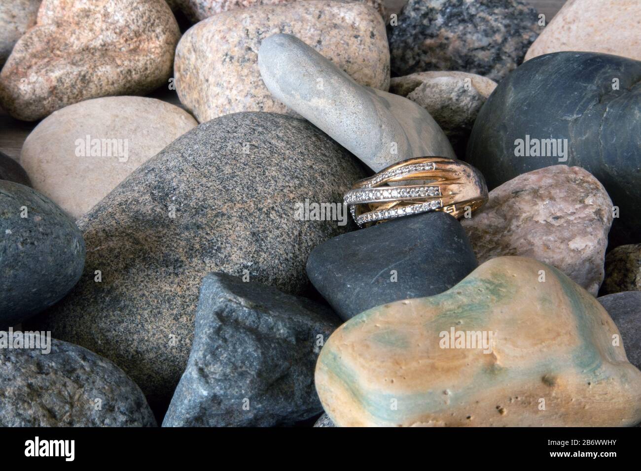 Goldener Ring mit vielen Zirkoniumsteinen, die auf einem Küsten-Kieselstein liegen Stockfoto