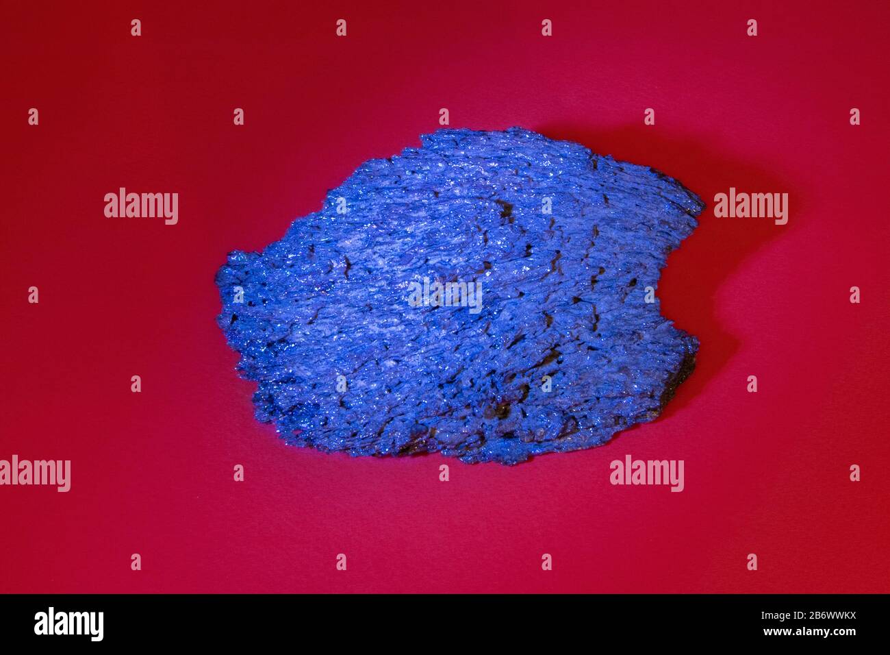 Großes Stück blaues schwarzes massives facettiertes Mineralkorund isoliert auf dunkelrotem Hintergrund Stockfoto