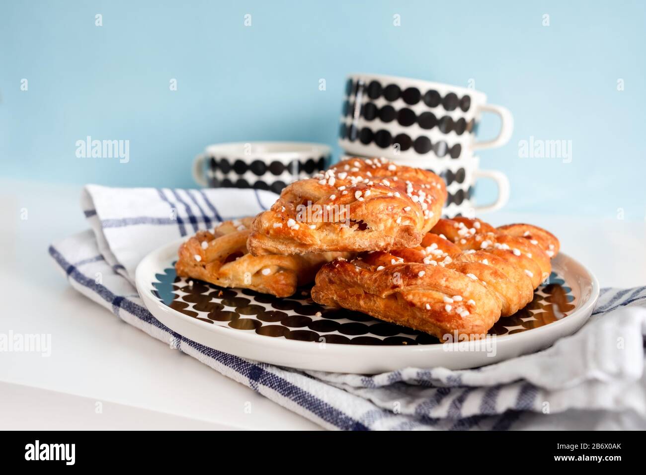 Frühstückseinrichtung mit dänischem Gebäck und Kaffeetassen, die auf weichem, blauem Hintergrund gefüllt werden können. Stockfoto