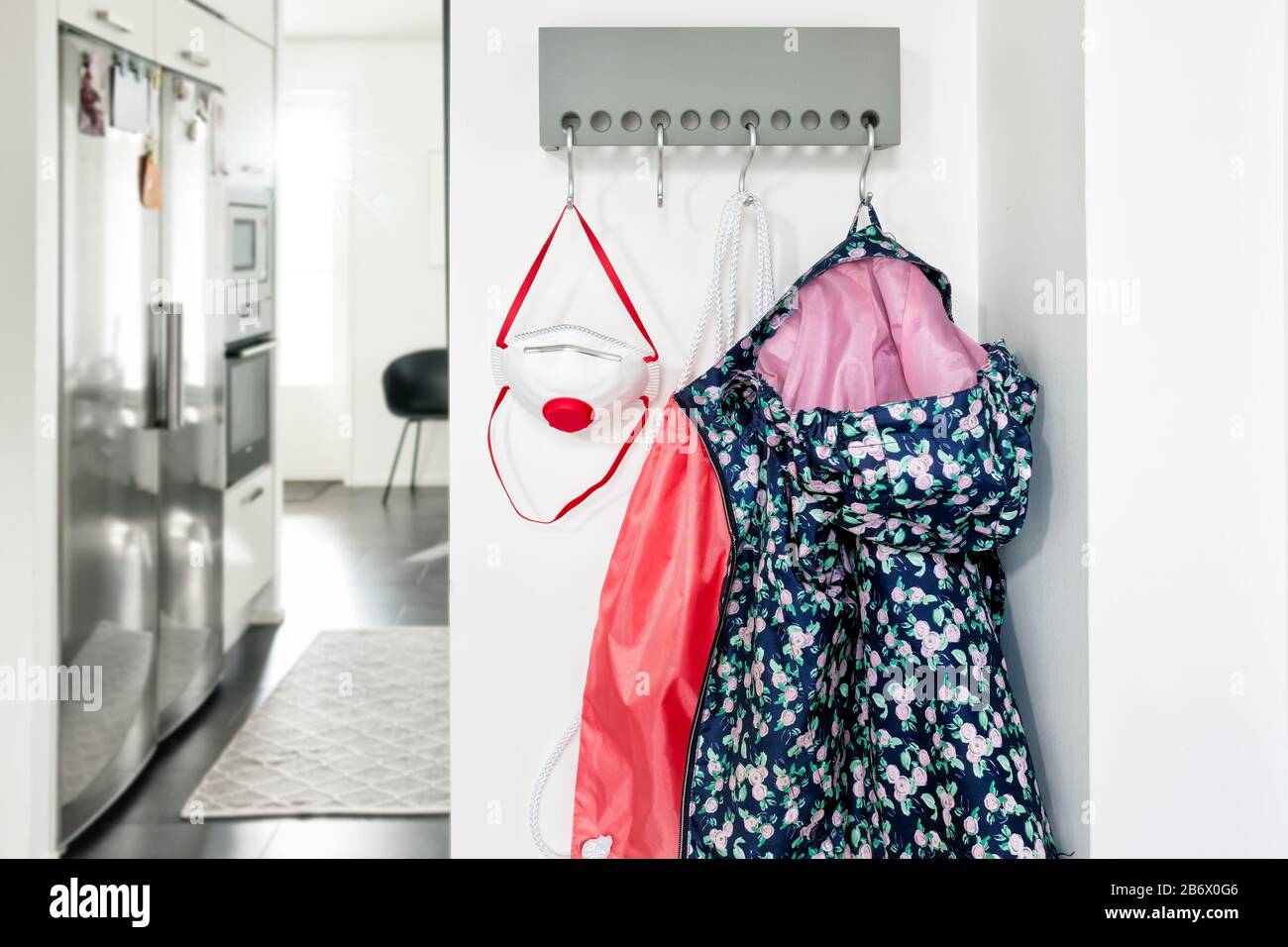 Wandmontiertes Kleiderregal in der Eingangshalle, an dem Jacke, Tasche und Atemschutzmaske des Mädchens hängen. Stockfoto