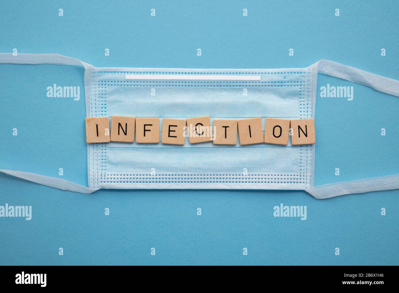 Schützende medizinische Gesichtsmaske mit dem Wort Infektion auf blauem Hintergrund Stockfoto
